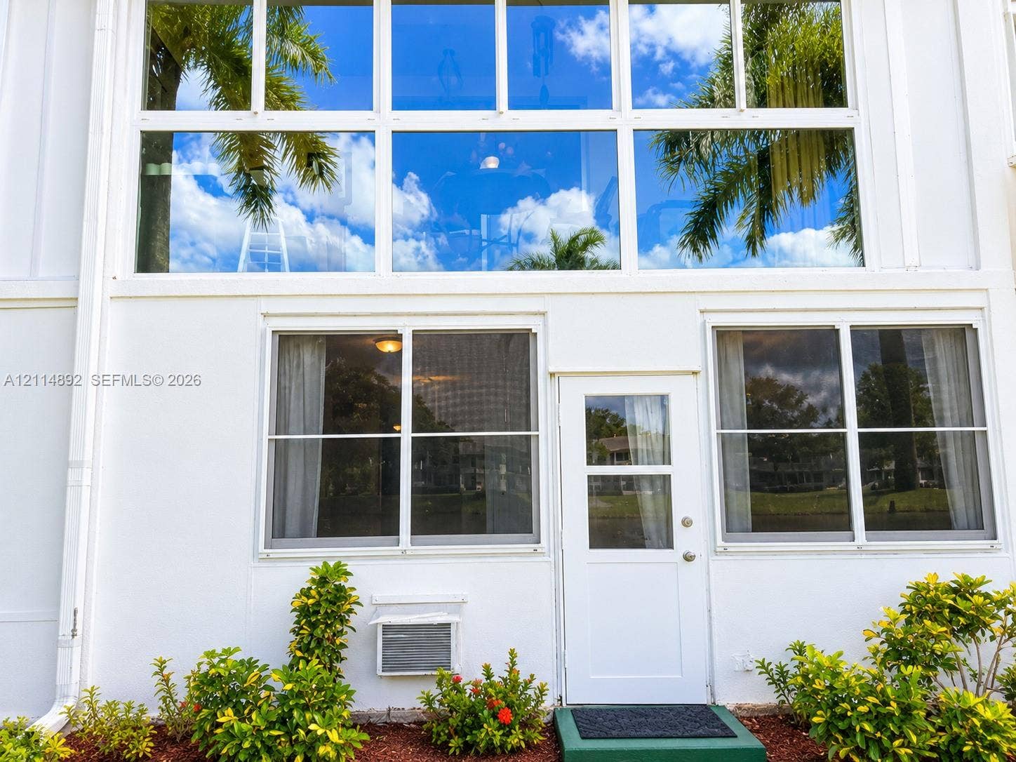 582 Durham U, #582, Deerfield Beach, FL 33442 Exterior facade featuring multi-pane floor-to-ceiling windows, white siding, and a pedestrian door with a glass insert, complemented by foundation landscaping
