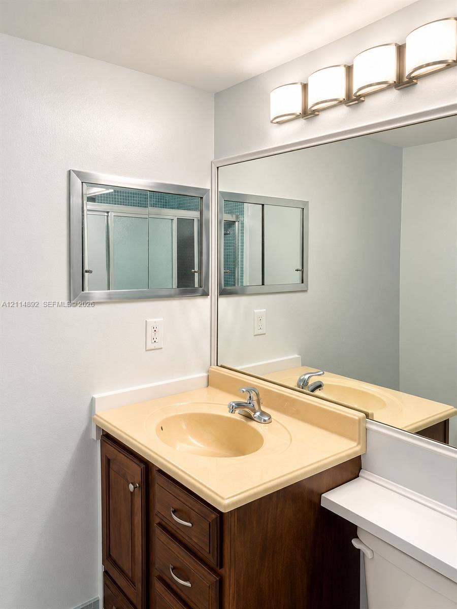 582 Durham U, #582, Deerfield Beach, FL 33442 Vanity featuring a wood-finish cabinet, molded countertop with integrated basin, polished metal faucet, wall-to-wall mirror, and four-light vanity fixture