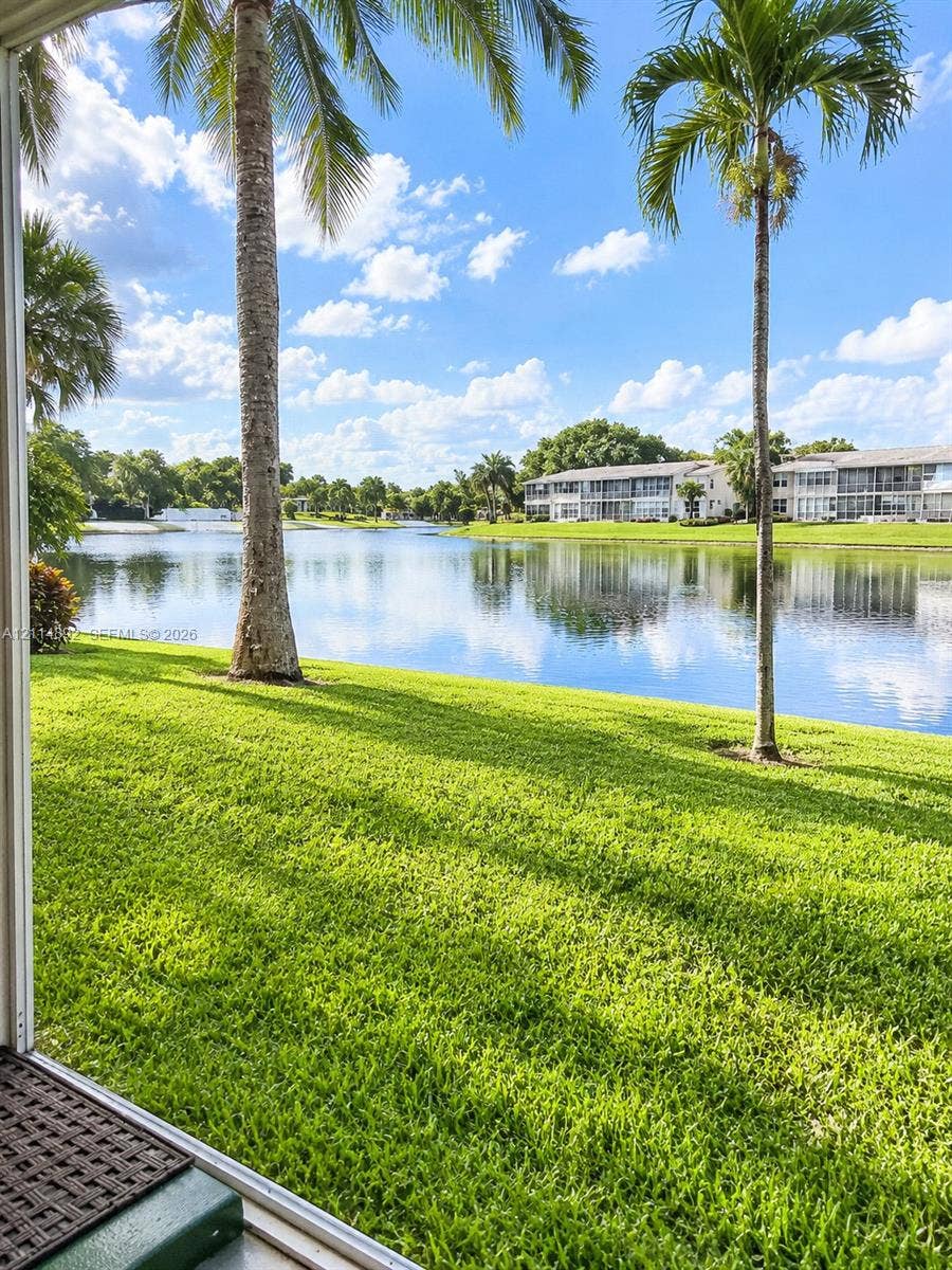 582 Durham U, #582, Deerfield Beach, FL 33442 Waterfront grounds featuring a grass lawn, mature palm trees, and a lake