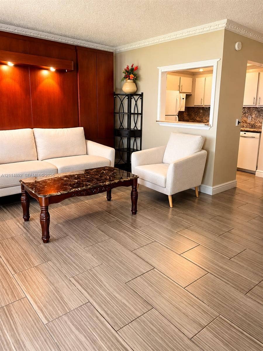 582 Durham U, #582, Deerfield Beach, FL 33442 Living area featuring wood-finish tile flooring, decorative crown molding, a wood-paneled accent wall with integrated recessed lighting, and a service pass-through window