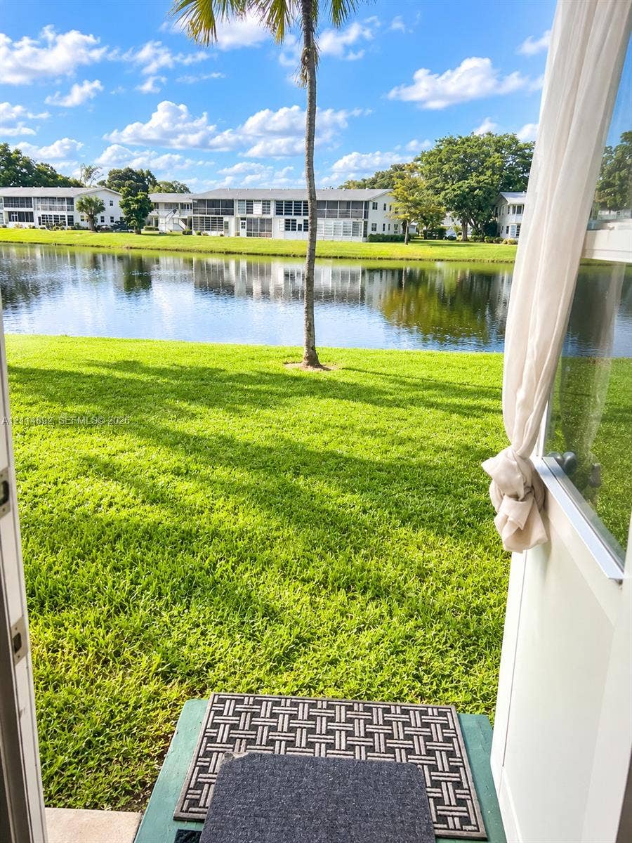 582 Durham U, #582, Deerfield Beach, FL 33442 Waterfront property featuring a manicured lawn, pond frontage, and mature palm tree