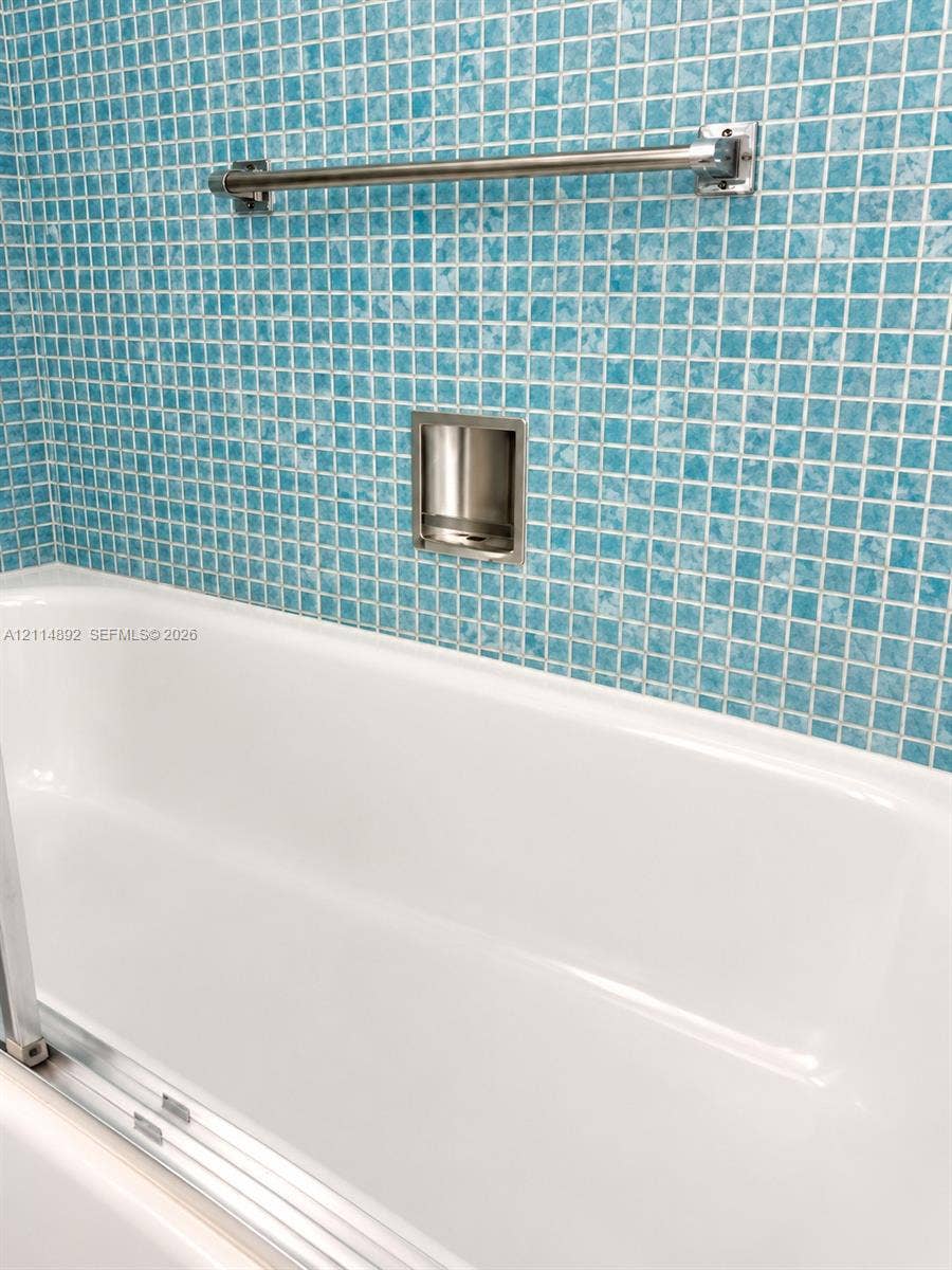 582 Durham U, #582, Deerfield Beach, FL 33442 White bathtub with integrated glass door track, complemented by blue mosaic tile surround, built-in recessed soap niche, and polished metal towel bar