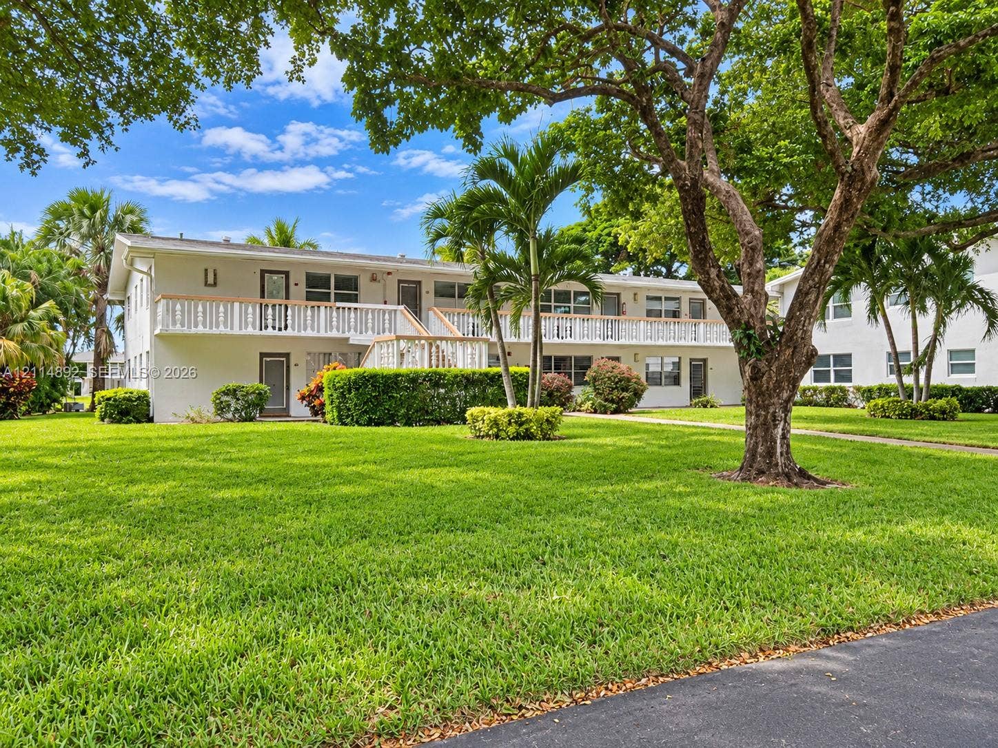 582 Durham U, #582, Deerfield Beach, FL 33442 Multi-level exterior featuring a second-story balcony with railings, manicured lawn, established landscaping, and mature trees