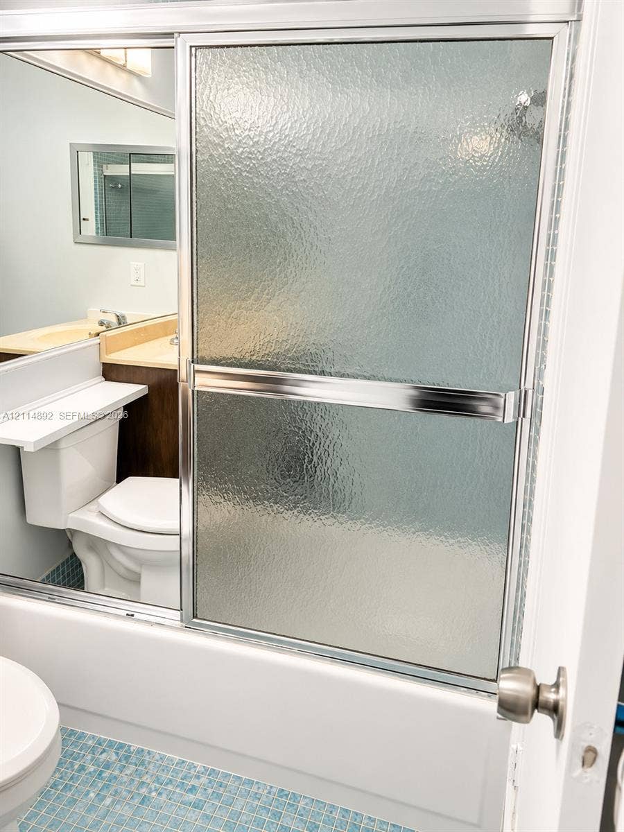 582 Durham U, #582, Deerfield Beach, FL 33442 Shower enclosure featuring textured glass sliding doors with chrome framing, blue mosaic tile flooring, and a vanity with a recessed sink