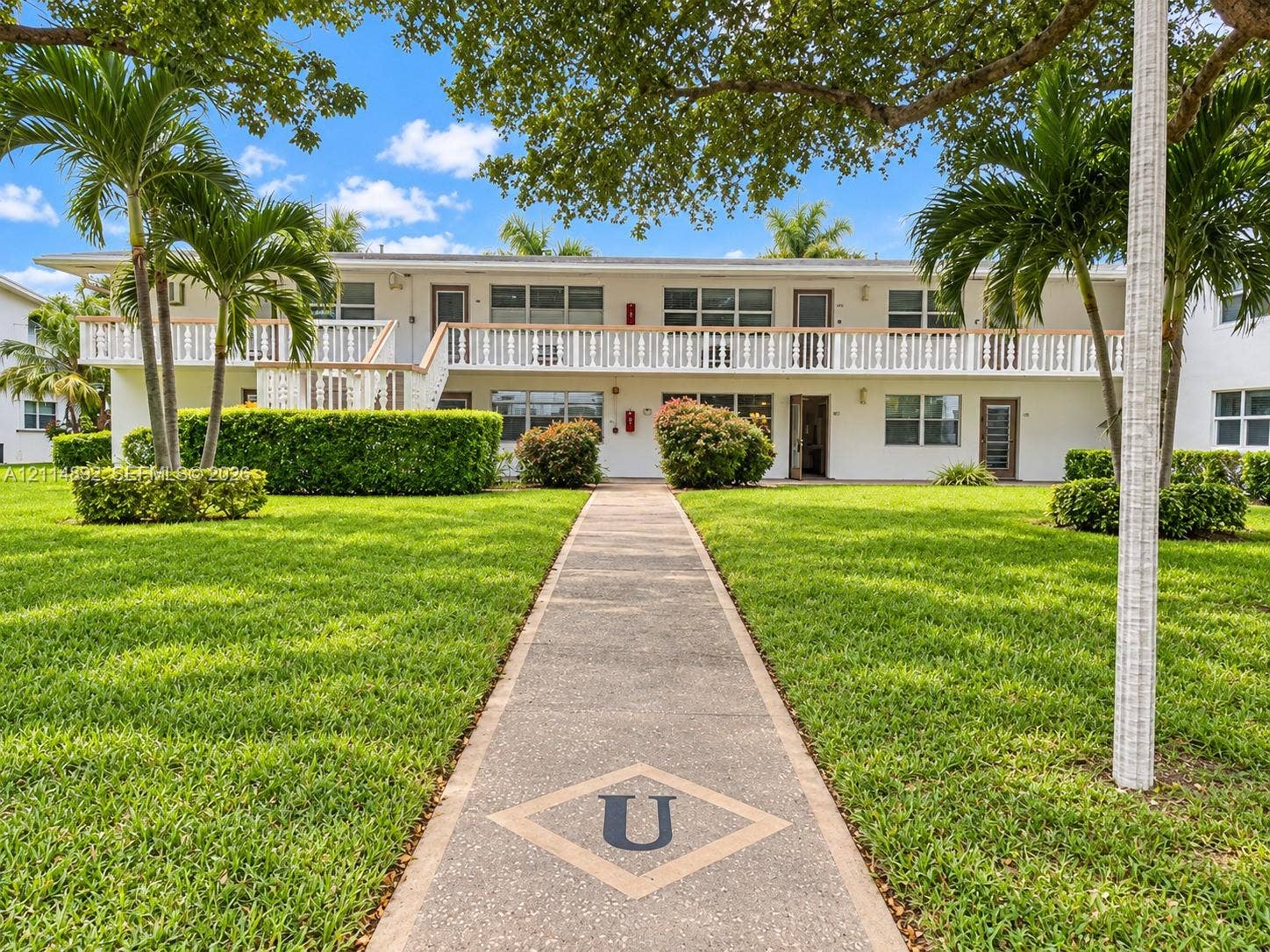 582 Durham U, #582, Deerfield Beach, FL 33442 Two-story exterior featuring a decorative second-level balcony, paved walkway, manicured lawn, and mature landscaping