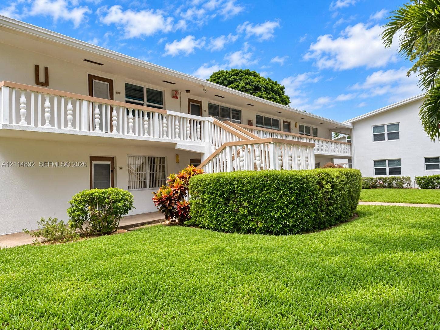 582 Durham U, #582, Deerfield Beach, FL 33442 Two-story exterior featuring white stucco siding, a second-level balcony with decorative balustrades, an open-air staircase, and manicured landscaping