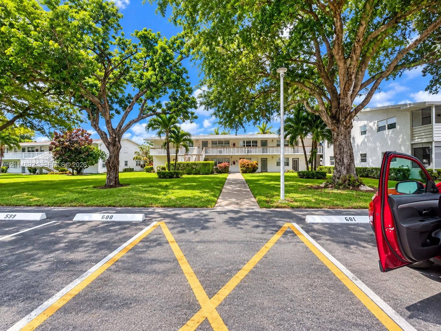 582 Durham U, #582, Deerfield Beach, FL 33442 Multi-story building exterior with white siding, second-level railed balcony, asphalt parking area, and mature landscaping