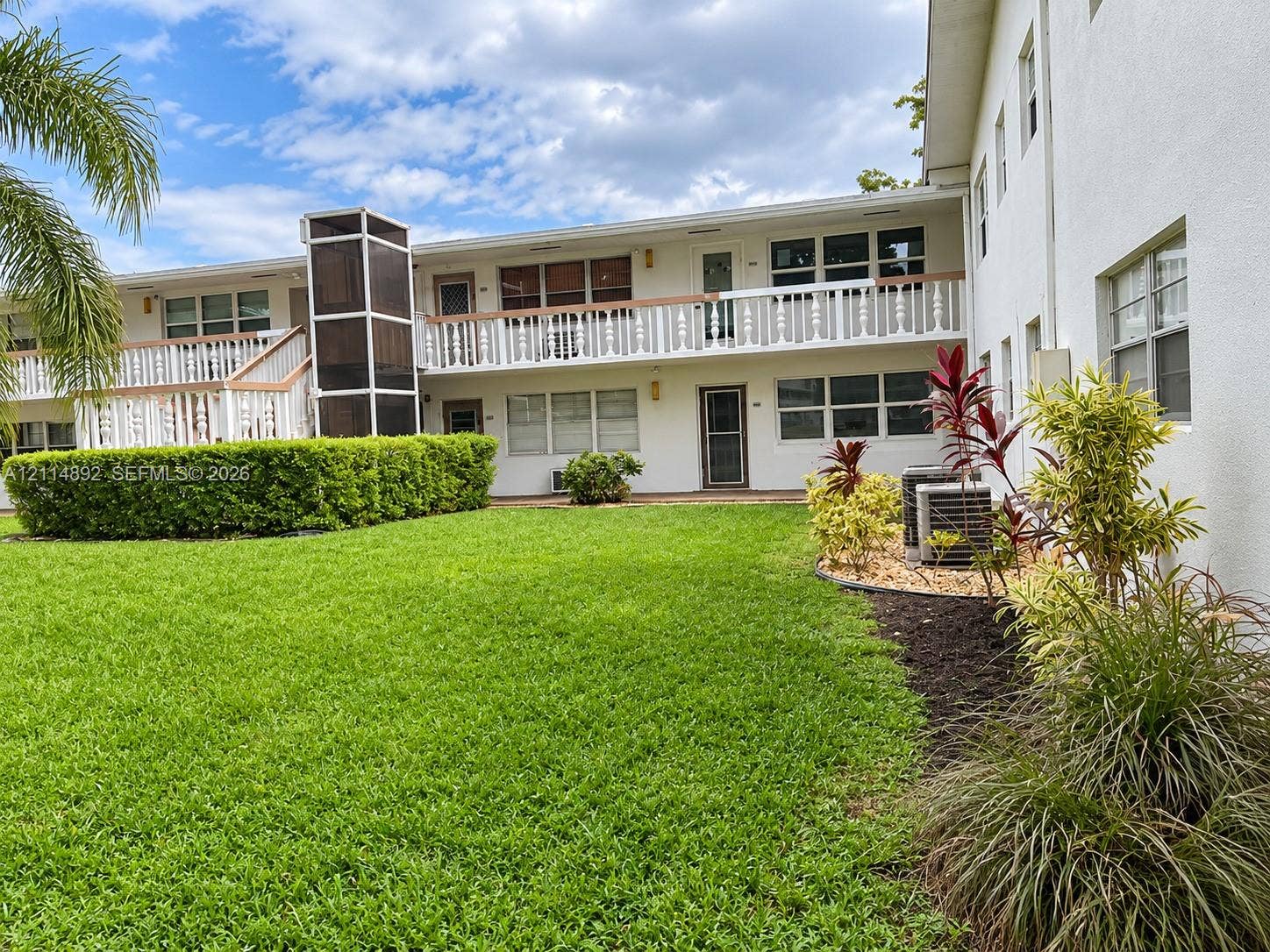 582 Durham U, #582, Deerfield Beach, FL 33442 Two-story exterior featuring white stucco siding, a wrap-around balcony with decorative balustrades, an integrated elevator shaft, and landscaped grounds with mature shrubbery