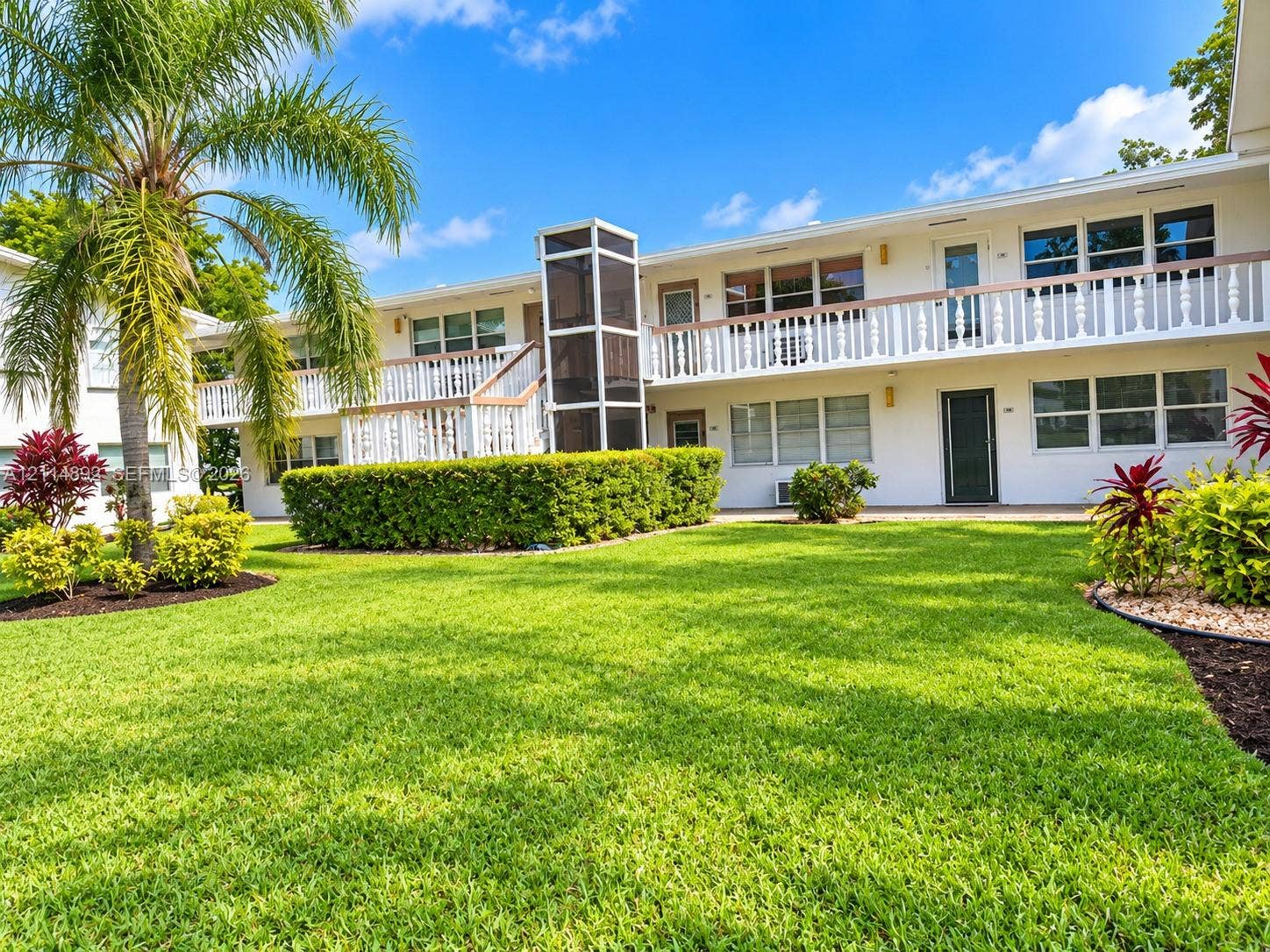 582 Durham U, #582, Deerfield Beach, FL 33442 Two-story exterior featuring white stucco siding, a second-level railed balcony, manicured lawn, and mature palm tree landscaping