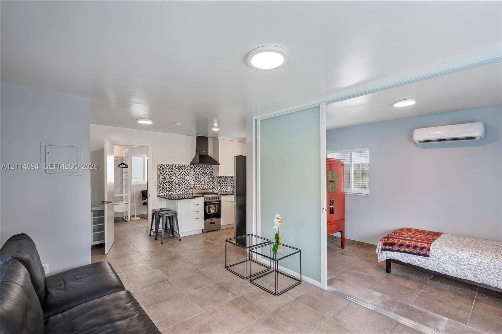 Large-format tile flooring, kitchen featuring patterned backsplash and stainless steel range, wall-mounted mini-split HVAC unit, and frosted glass sliding room divider