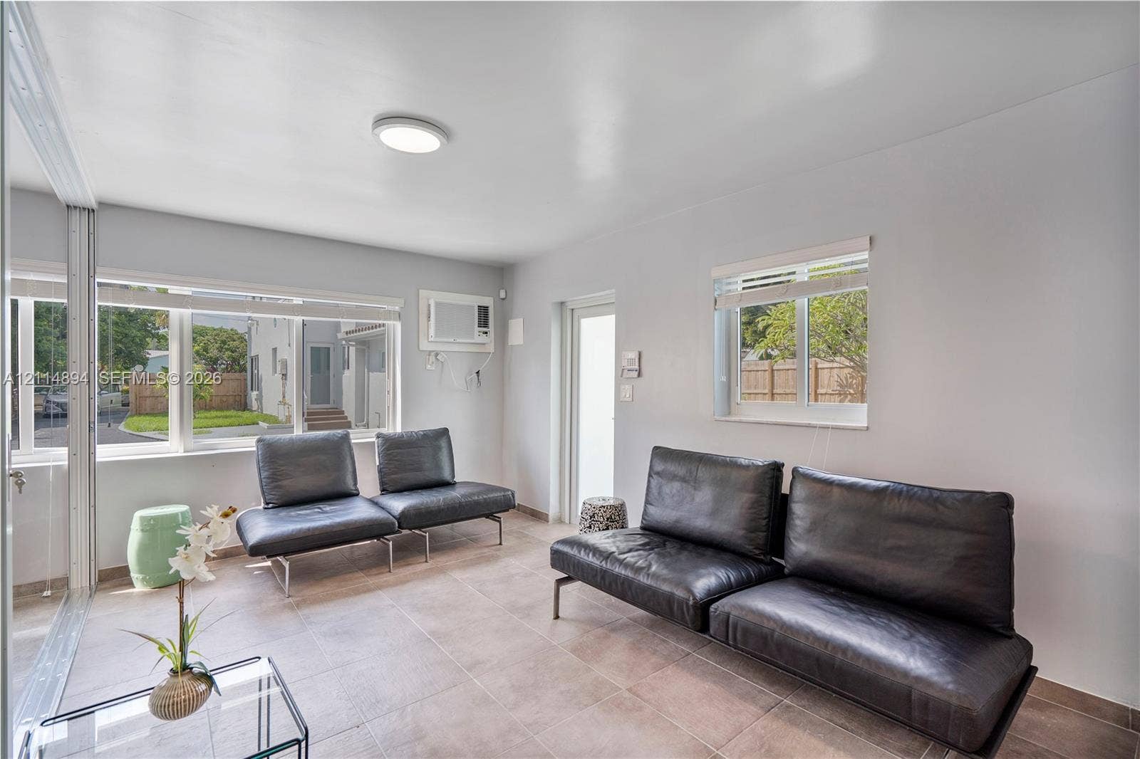 Neutral-toned room featuring large windows, stone-tile flooring, flush-mount lighting, and a wall-mounted air conditioning unit