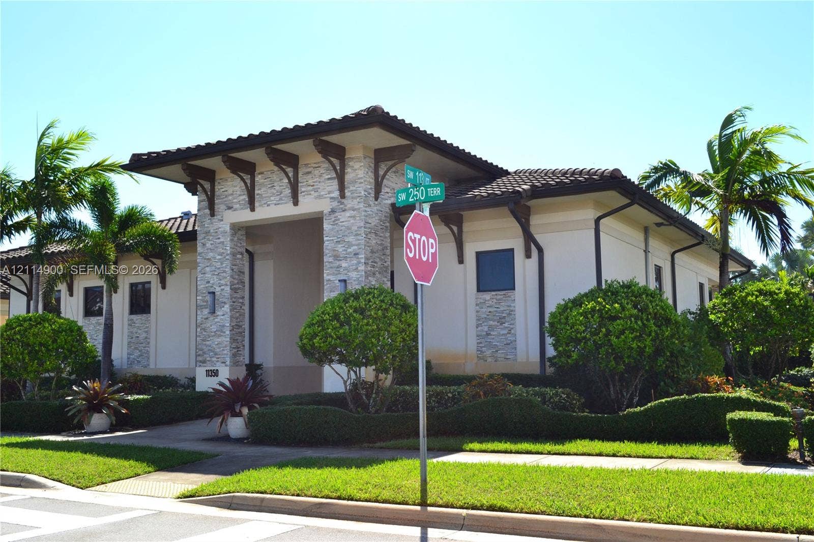 25048 SW 113th Place, Homestead, FL 33032 Single-story exterior featuring a stone-clad portico, decorative wooden roof corbels, low-pitched tiled roofing, and manicured landscaping