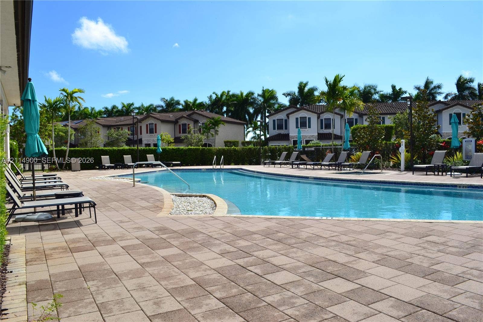 25048 SW 113th Place, Homestead, FL 33032 Swimming pool featuring a stone-paver deck, pebble-lined accent border, manicured hedges, and palm tree landscaping