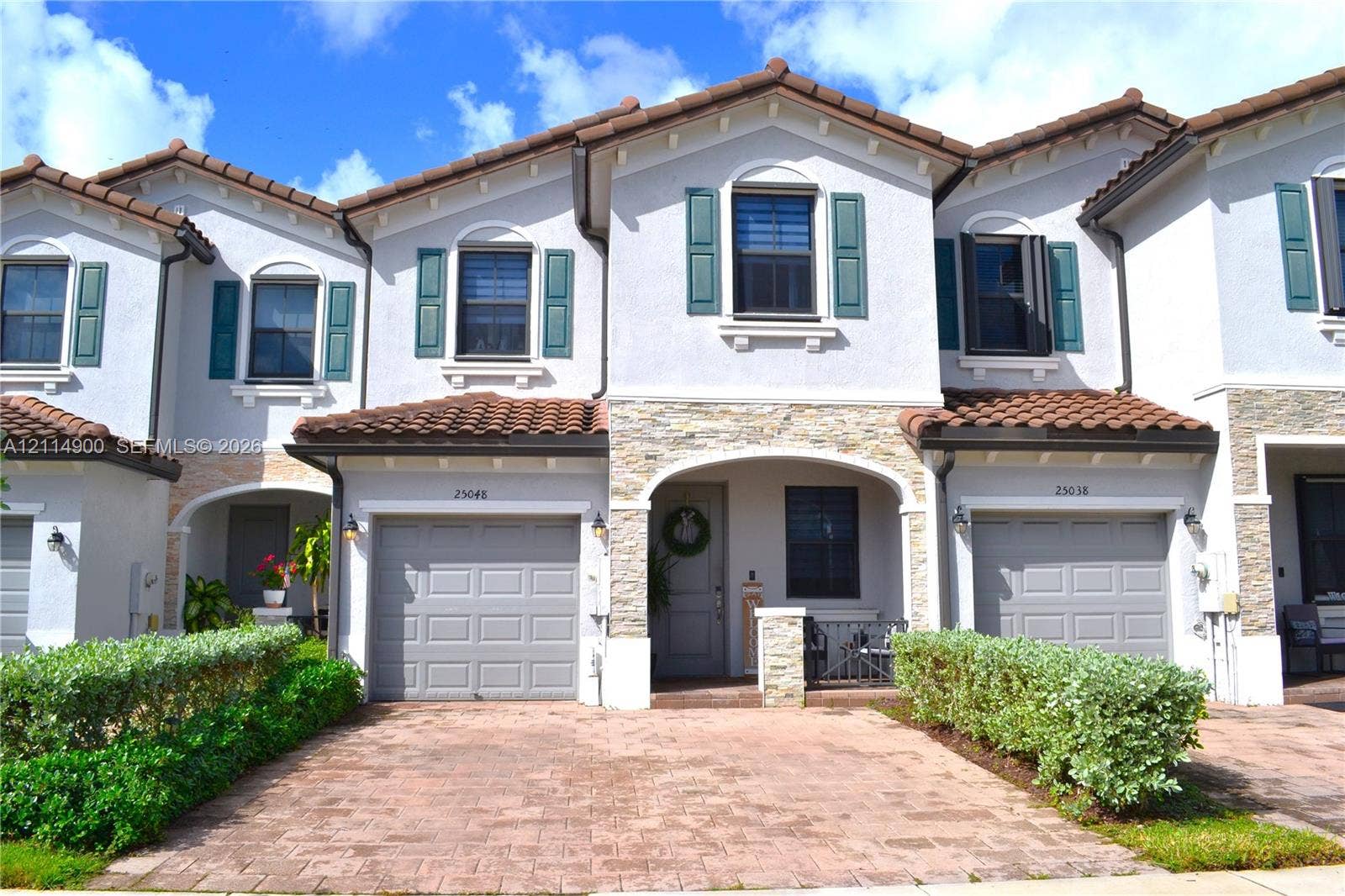 25048 SW 113th Place, Homestead, FL 33032 Multi-family exterior featuring a light-toned stucco facade with stone veneer accents, decorative shutters, a clay-tile roof, and a paved brick driveway