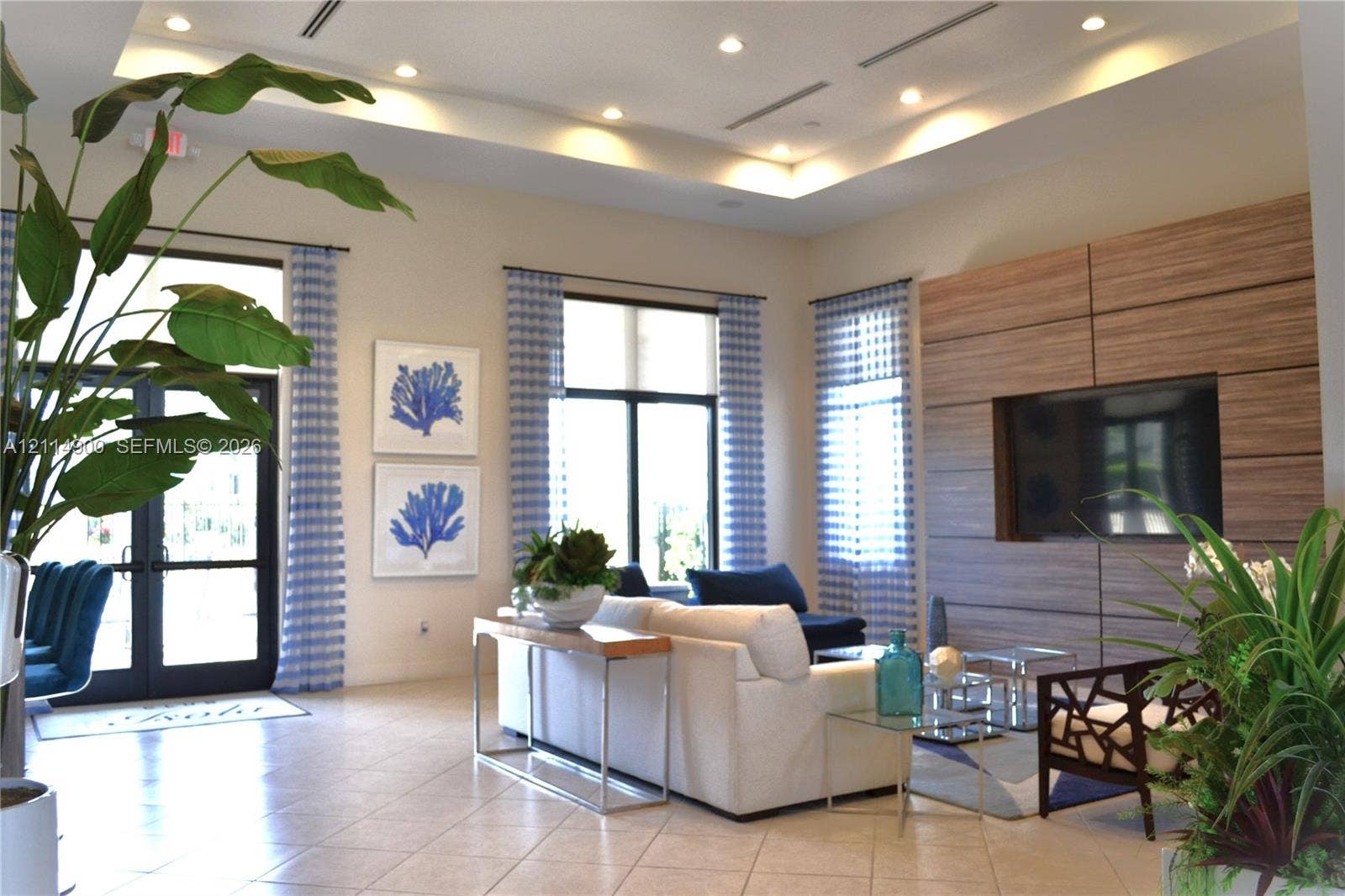 25048 SW 113th Place, Homestead, FL 33032 Open-concept living space featuring high tray ceilings with recessed lighting, large-format tile flooring, oversized windows, and a wood-panel accent wall with integrated media storage