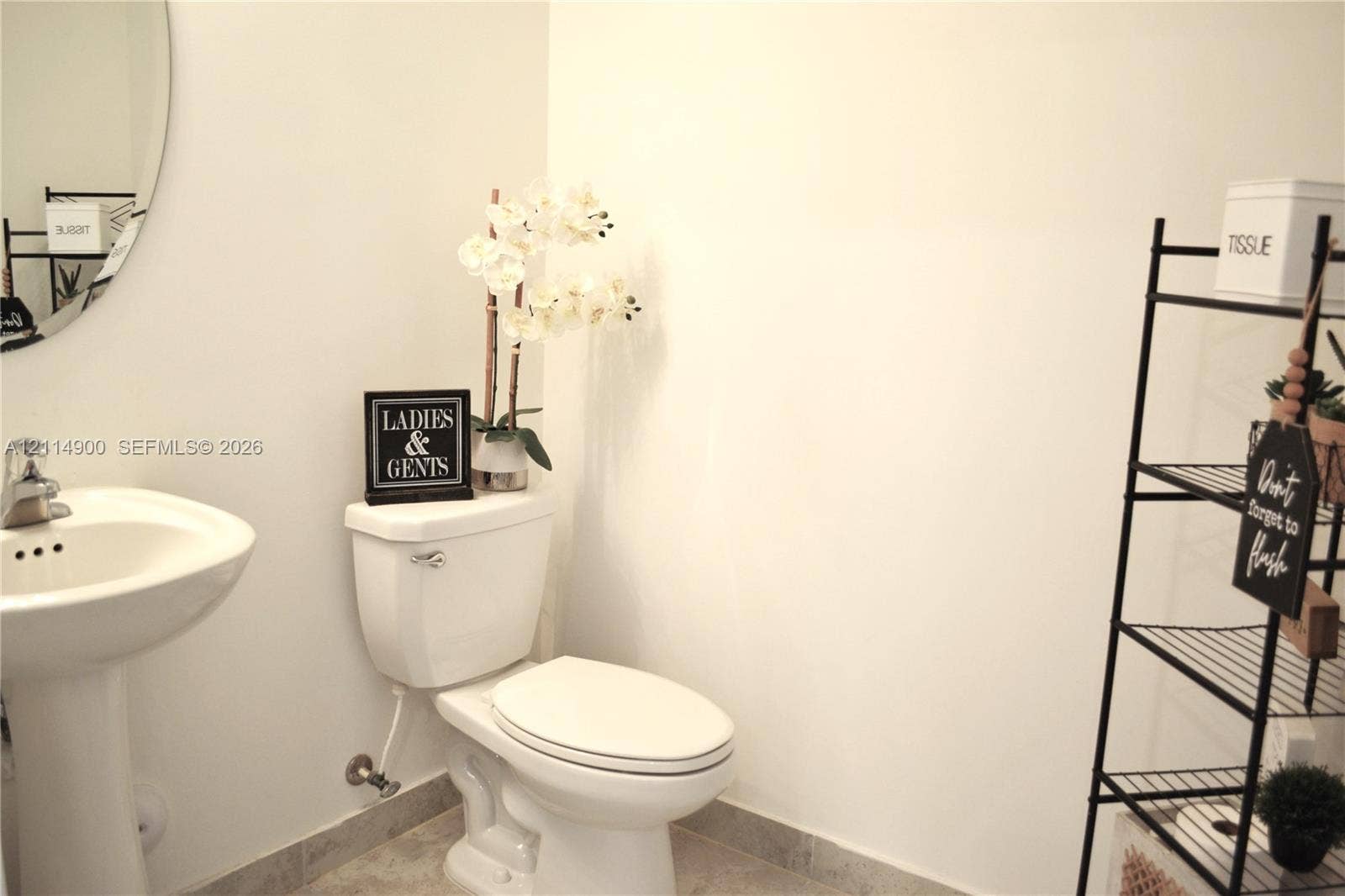 25048 SW 113th Place, Homestead, FL 33032 Pedestal sink featuring a polished chrome faucet and an oval wall-mounted mirror, paired with a standard-profile toilet and stone-finish flooring