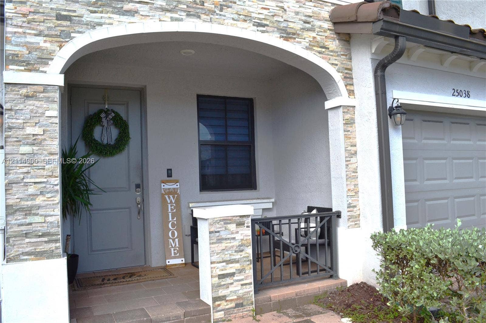 25048 SW 113th Place, Homestead, FL 33032 Covered entryway featuring a stone veneer facade, an arched architectural detail, a paver porch, and metal railing