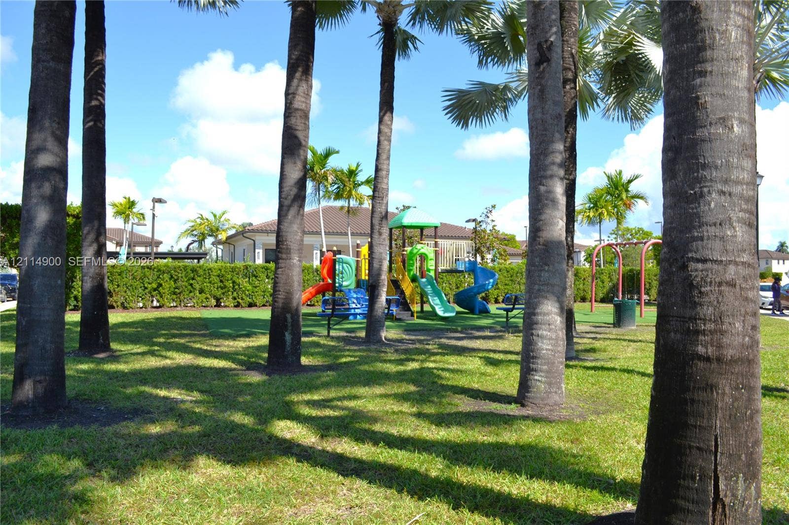 25048 SW 113th Place, Homestead, FL 33032 Outdoor recreational area featuring mature palm trees, manicured lawn, hedge landscaping, and a multi-component play structure