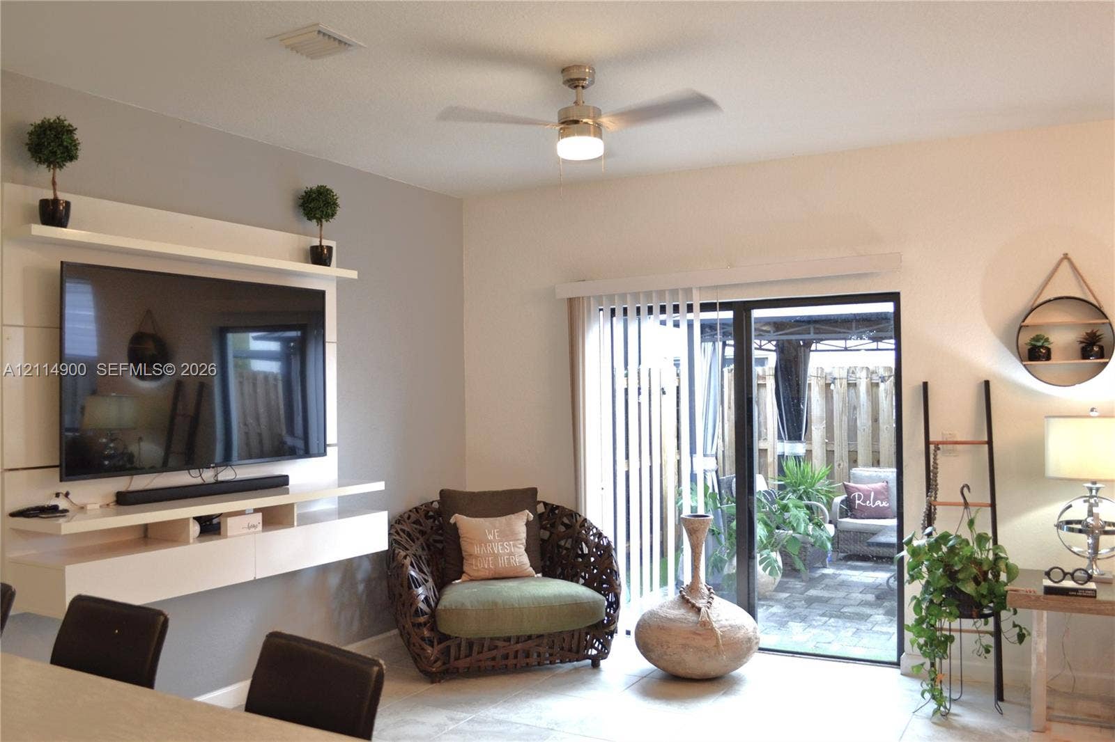 25048 SW 113th Place, Homestead, FL 33032 Living area featuring a custom white built-in media console with tiered shelving, sliding glass door with vertical blinds, and a ceiling-mounted light fixture with fan