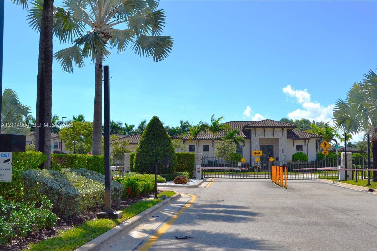 25048 SW 113th Place, Homestead, FL 33032 Gated community entrance featuring stone-accented architecture, tile roof, and professional landscaping with palm trees
