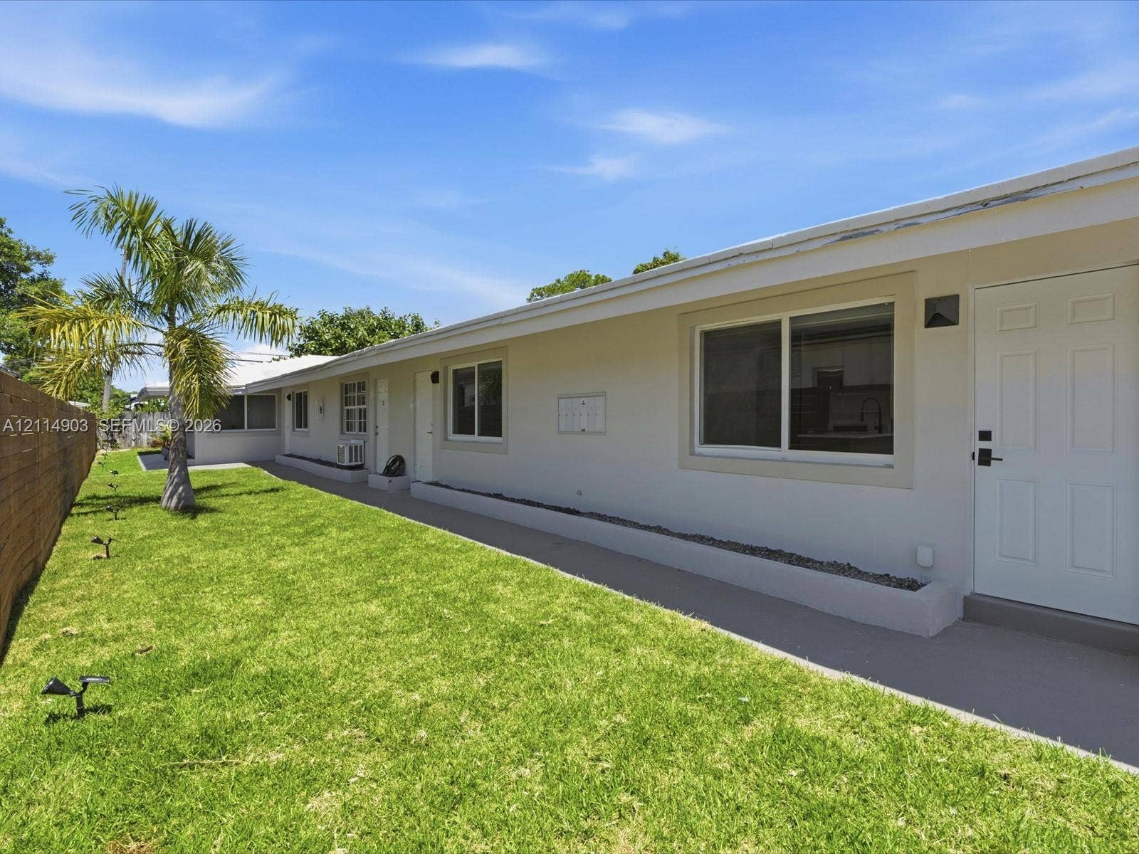 1129 NE 16th Avenue, #1, Fort Lauderdale, Fort Lauderdale, FL 33304 Exterior featuring a manicured lawn, palm tree, concrete pathway, and horizontal wood-slat fencing