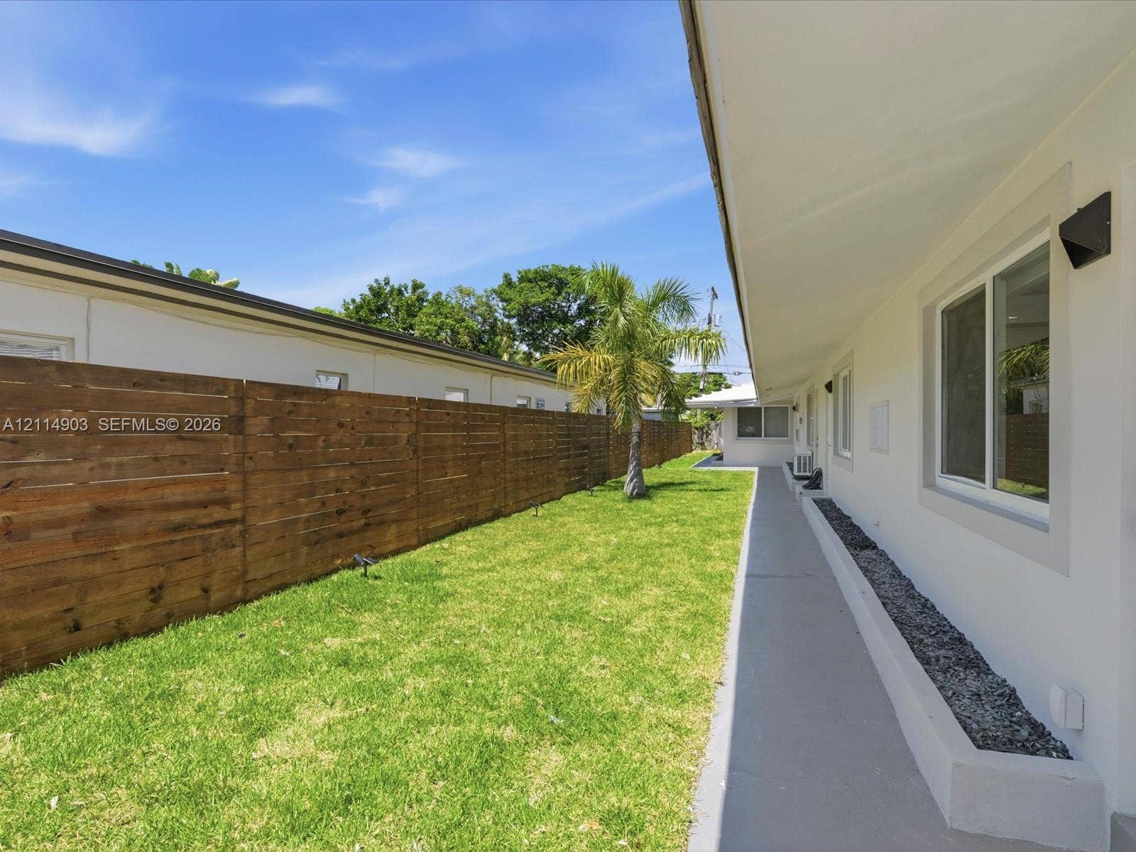 1129 NE 16th Avenue, #1, Fort Lauderdale, Fort Lauderdale, FL 33304 Exterior side yard featuring a concrete walkway, horizontal wood fencing, and a stone-filled planting border