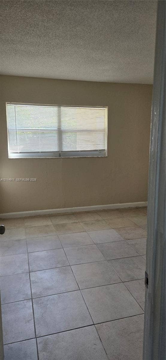 1045 Miami Boulevard, #A, Delray Beach, Delray Beach, FL 33483 Neutral-toned interior space featuring light-colored square tile flooring, a horizontal slider window, and textured ceiling finish