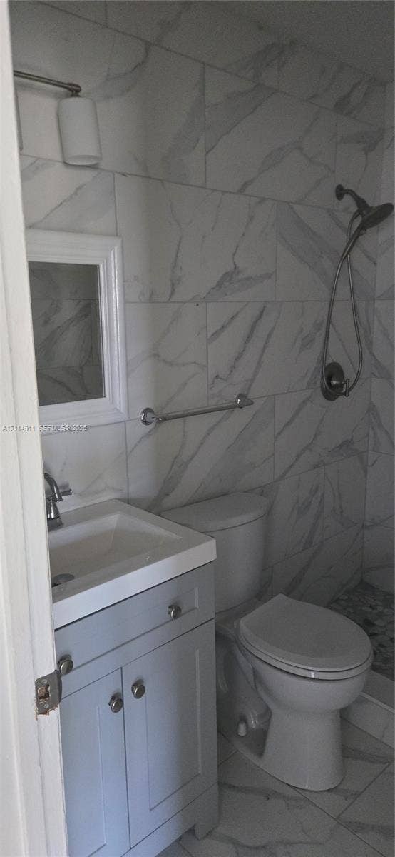 1045 Miami Boulevard, #A, Delray Beach, Delray Beach, FL 33483 Full-height stone-patterned wall tile, gray shaker-style vanity with white porcelain sink, chrome handheld shower fixture, and polished chrome hardware