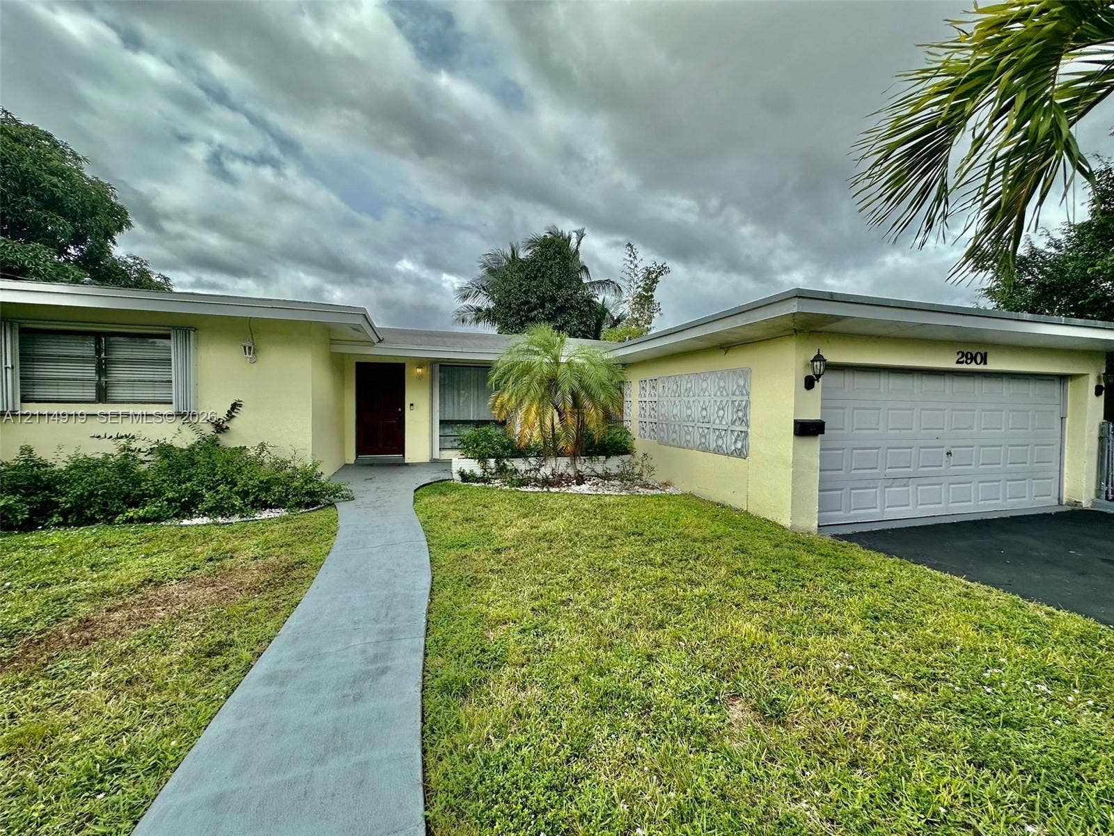 2901 NW 9th Terrace, #., Wilton Manors, Wilton Manors, FL 33311 Single-story residence featuring a concrete walkway, attached two-car garage, decorative exterior masonry screen, and mature landscape plantings