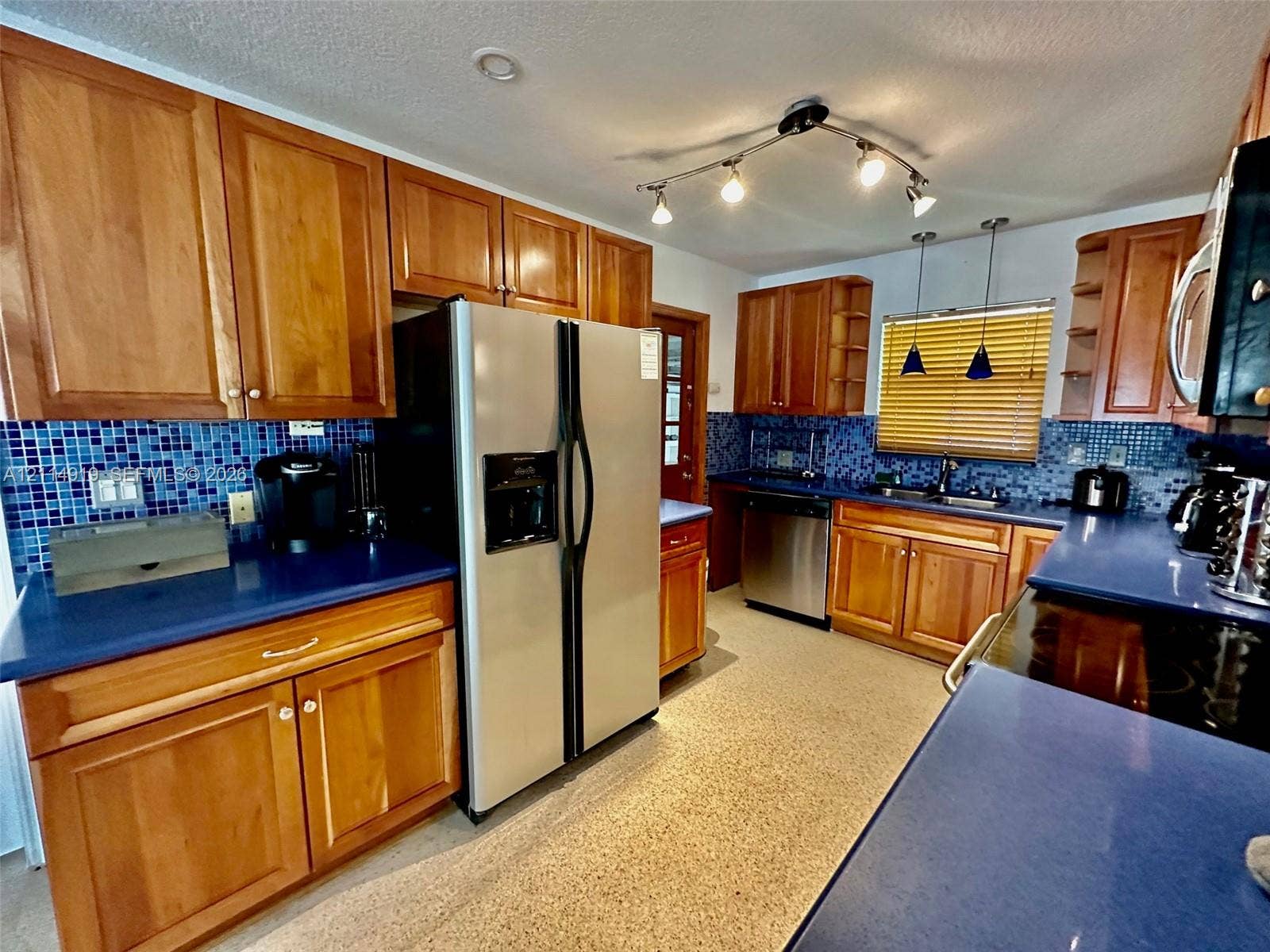 2901 NW 9th Terrace, #., Wilton Manors, Wilton Manors, FL 33311 Kitchen featuring warm-tone wood cabinetry, blue solid-surface countertops, a mosaic tile backsplash, stainless steel appliances, and track lighting