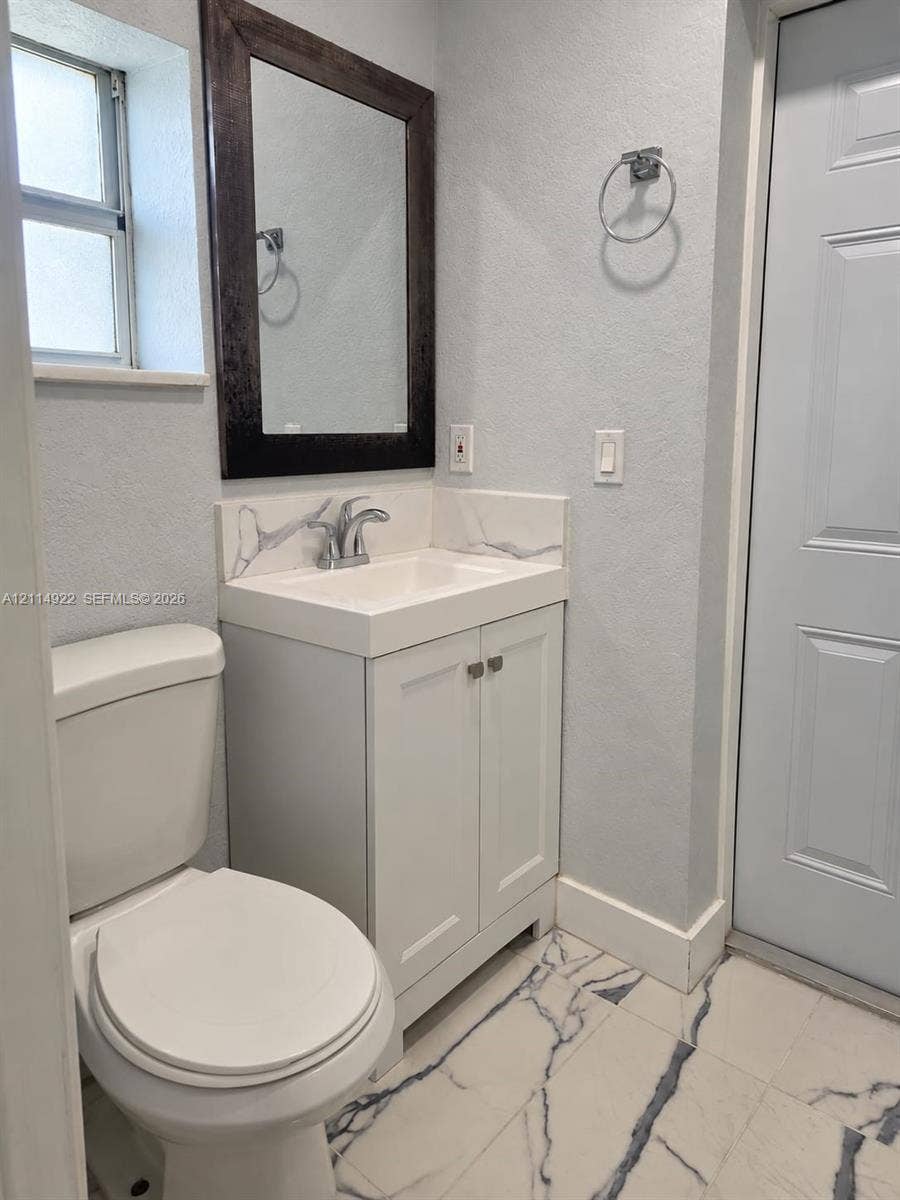 16201 SW 169th Avenue, #C, Miami, Miami, FL 33187 White vanity featuring a solid surface countertop with integrated sink and backsplash, dark-framed wall mirror, and patterned tile flooring
