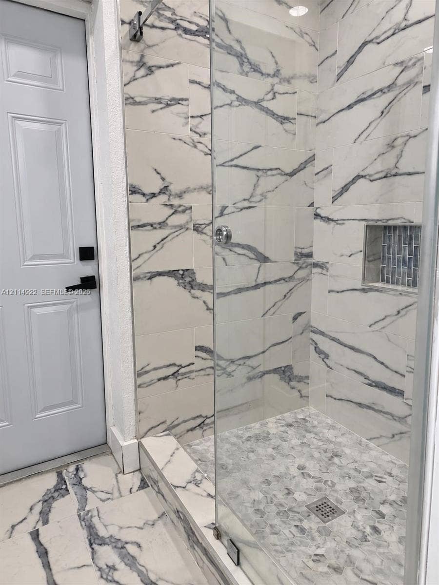 16201 SW 169th Avenue, #C, Miami, Miami, FL 33187 Walk-in shower featuring large-format veined tile surround, glass enclosure, pebble-stone flooring, built-in recessed niche with mosaic accent tile, and matte black door hardware