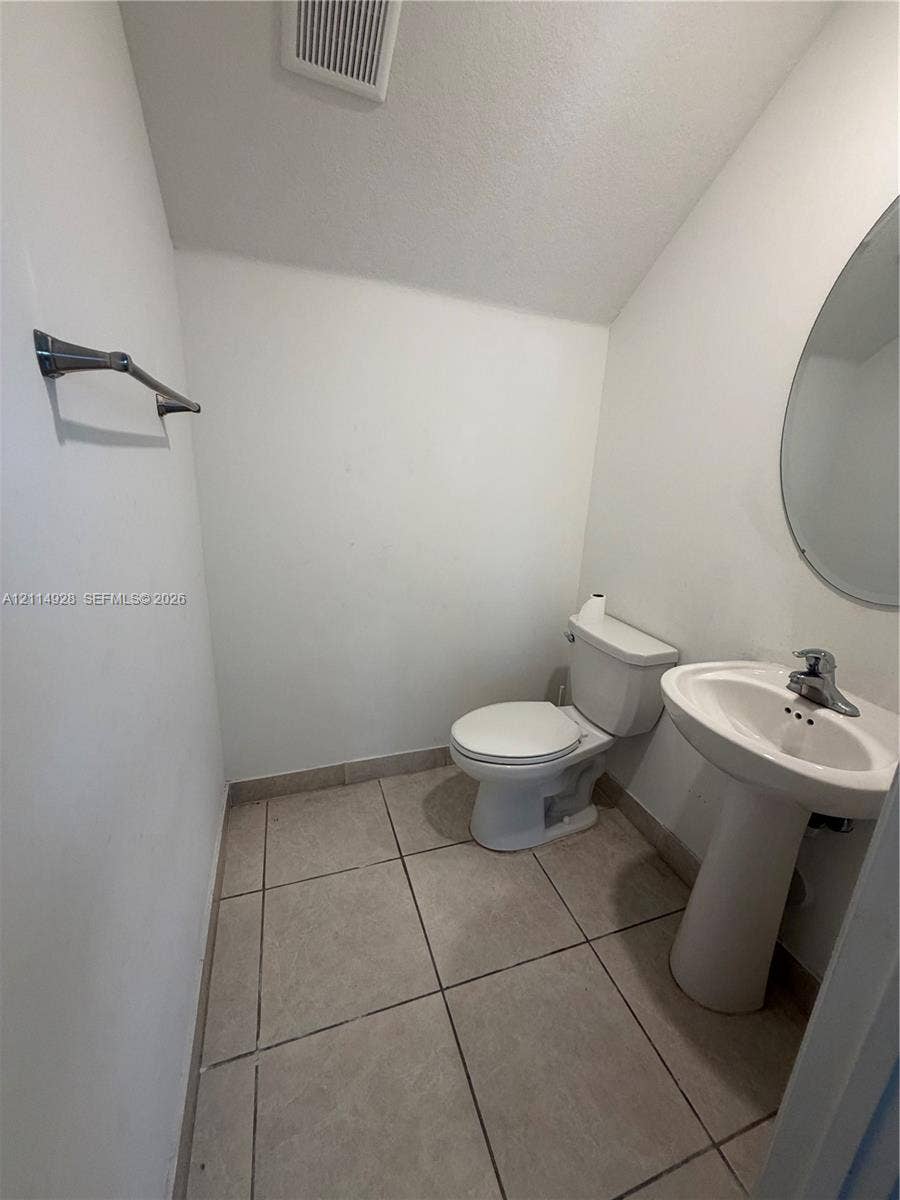 1411 SE 26th Road, Homestead, FL 33035 Powder room featuring tile flooring, a pedestal sink with a chrome single-handle faucet, an oval wall-mounted mirror, and a chrome towel bar