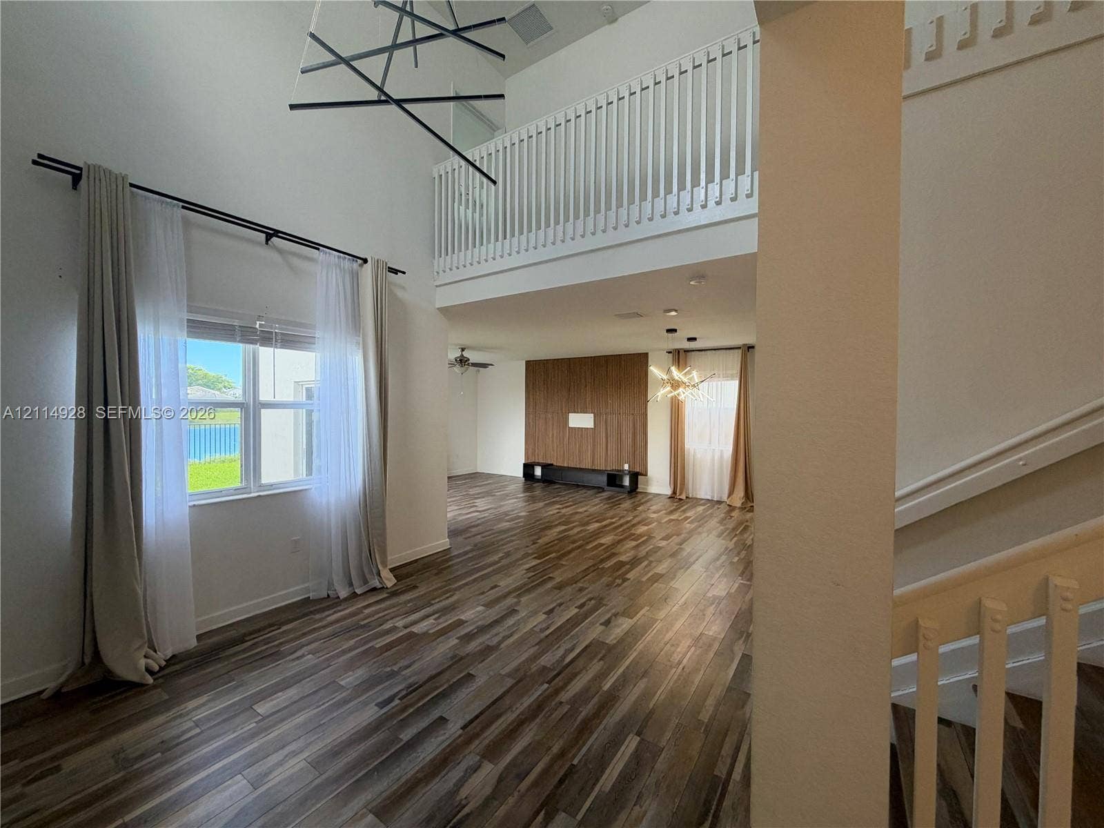 1411 SE 26th Road, Homestead, FL 33035 Double-height ceiling with geometric chandelier, wood-finish flooring, second-level balcony railing, and wood-paneled accent wall