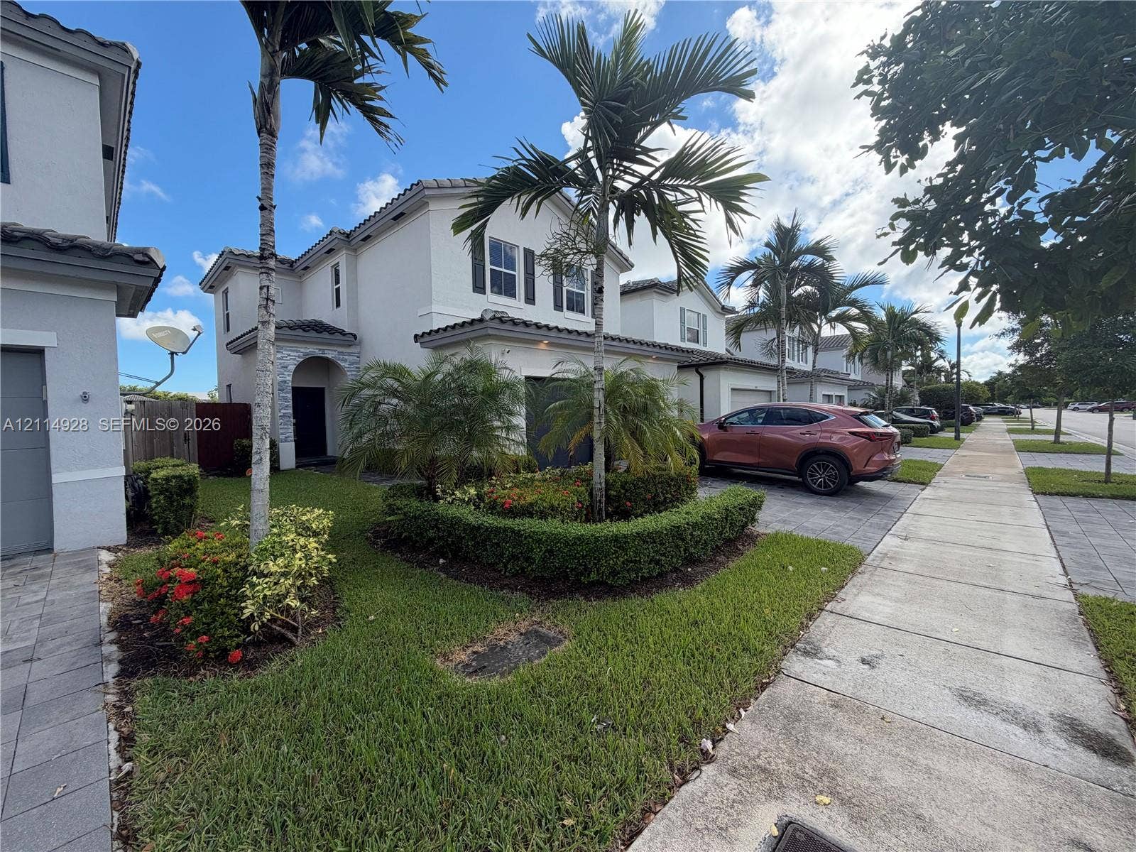 1411 SE 26th Road, Homestead, FL 33035 Two-story exterior featuring a light-colored stucco facade, decorative stone detailing at the entryway, shutter-framed windows, and professional landscaping with palm trees