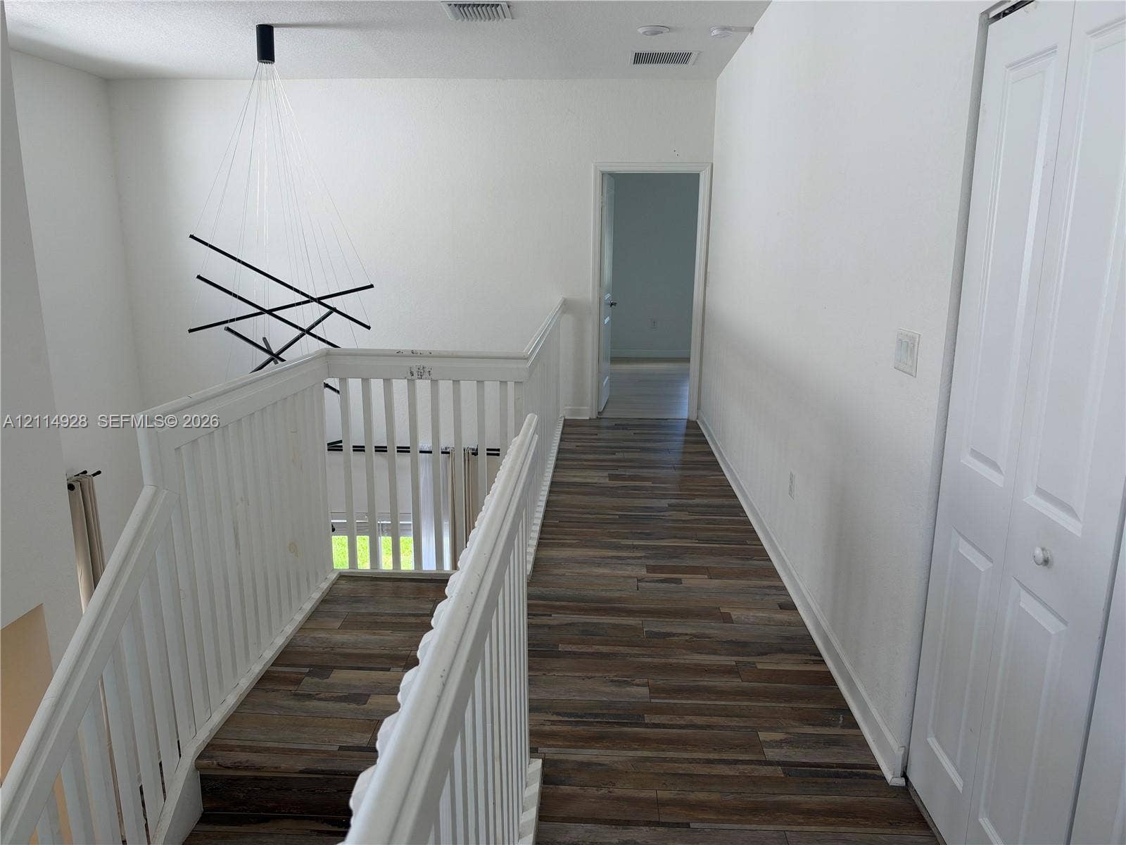 1411 SE 26th Road, Homestead, FL 33035 Hallway featuring wood-finish flooring, white railing, modern multi-rod pendant lighting, and a bifold closet