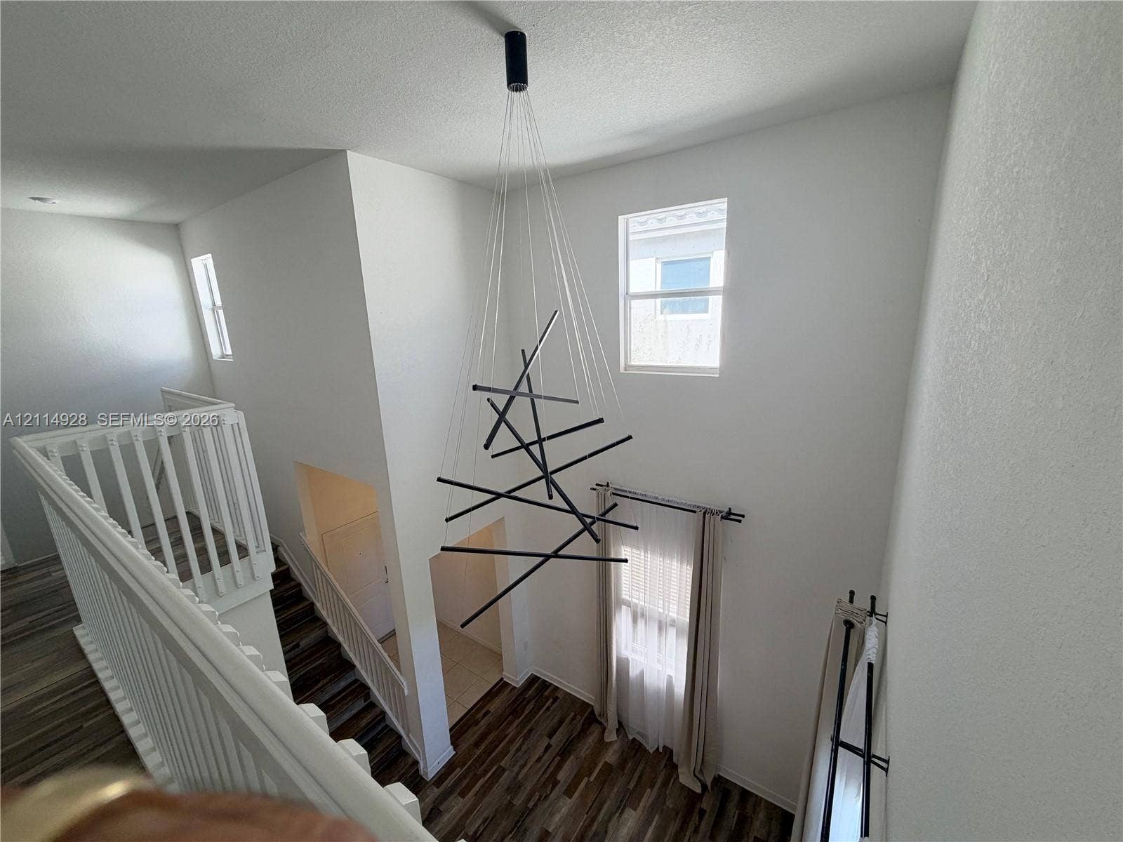 1411 SE 26th Road, Homestead, FL 33035 Two-story foyer featuring high ceilings, wood-finish flooring, a contemporary geometric multi-light chandelier, and white wooden balustrades