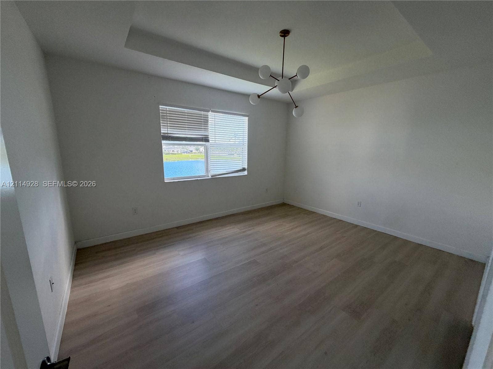1411 SE 26th Road, Homestead, FL 33035 Tray ceiling, modern multi-arm chandelier, wood-finish flooring, and horizontal window blinds