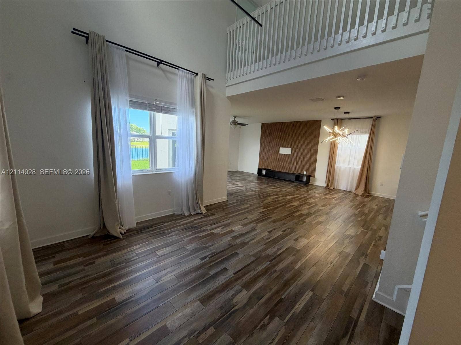 1411 SE 26th Road, Homestead, FL 33035 Interior featuring double-height ceilings, wood-finish flooring, a wood-panel accent wall, and a slatted staircase railing