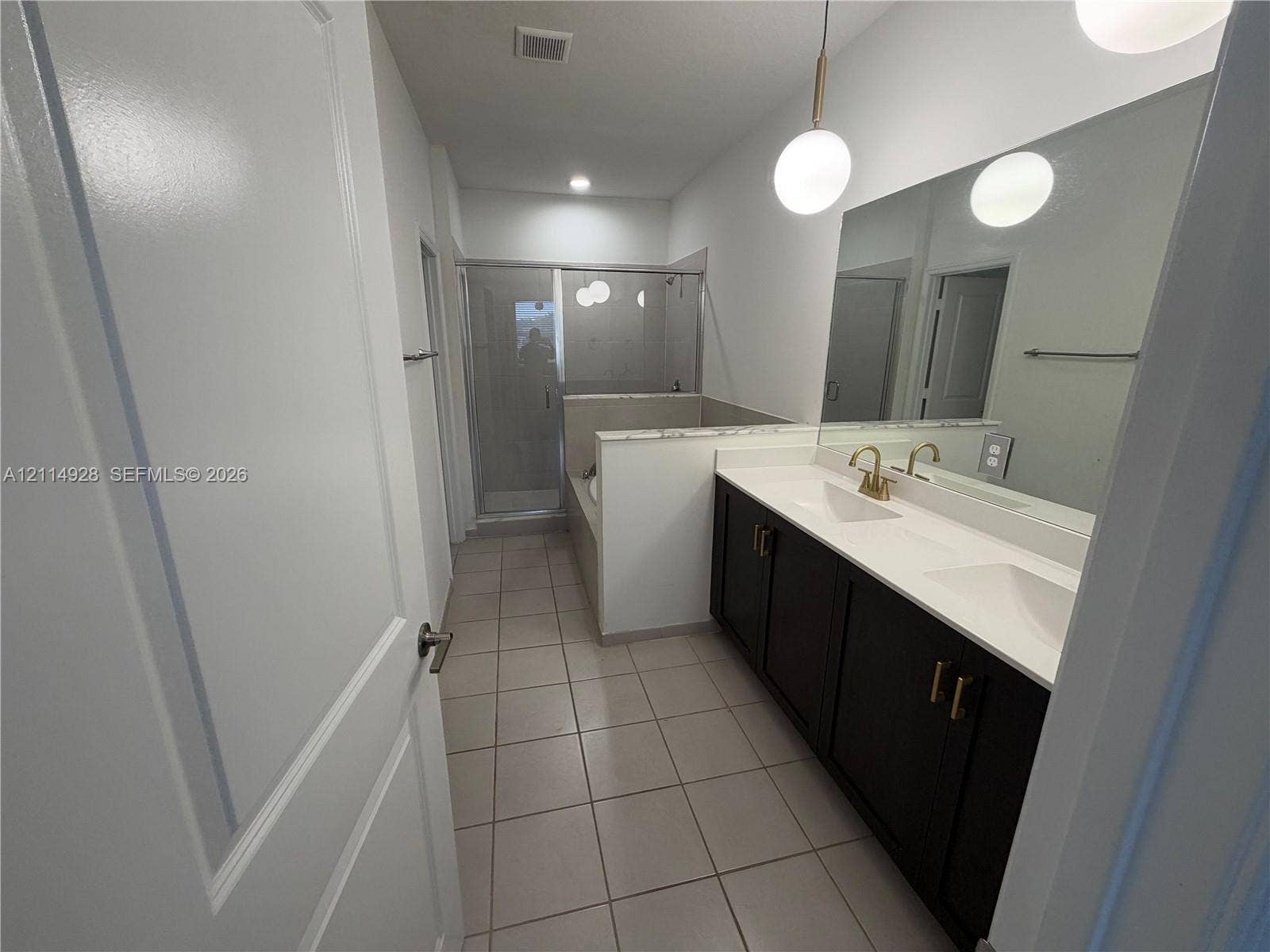 1411 SE 26th Road, Homestead, FL 33035 Dual-sink vanity with dark cabinetry and white countertops, pendant globe lighting, large wall-mounted mirror, ceramic tile flooring, and a glass-enclosed shower with a soaking tub