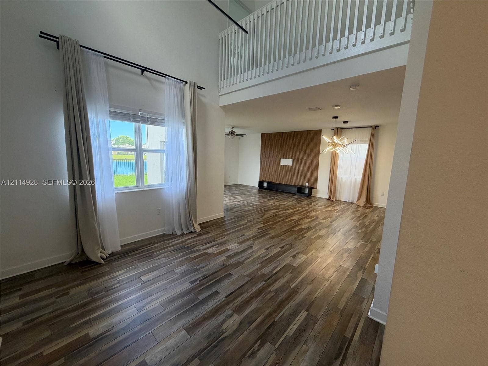 1411 SE 26th Road, Homestead, FL 33035 Double-height ceiling, wood-finish flooring, built-in wooden wall paneling, and a balcony with a white railing