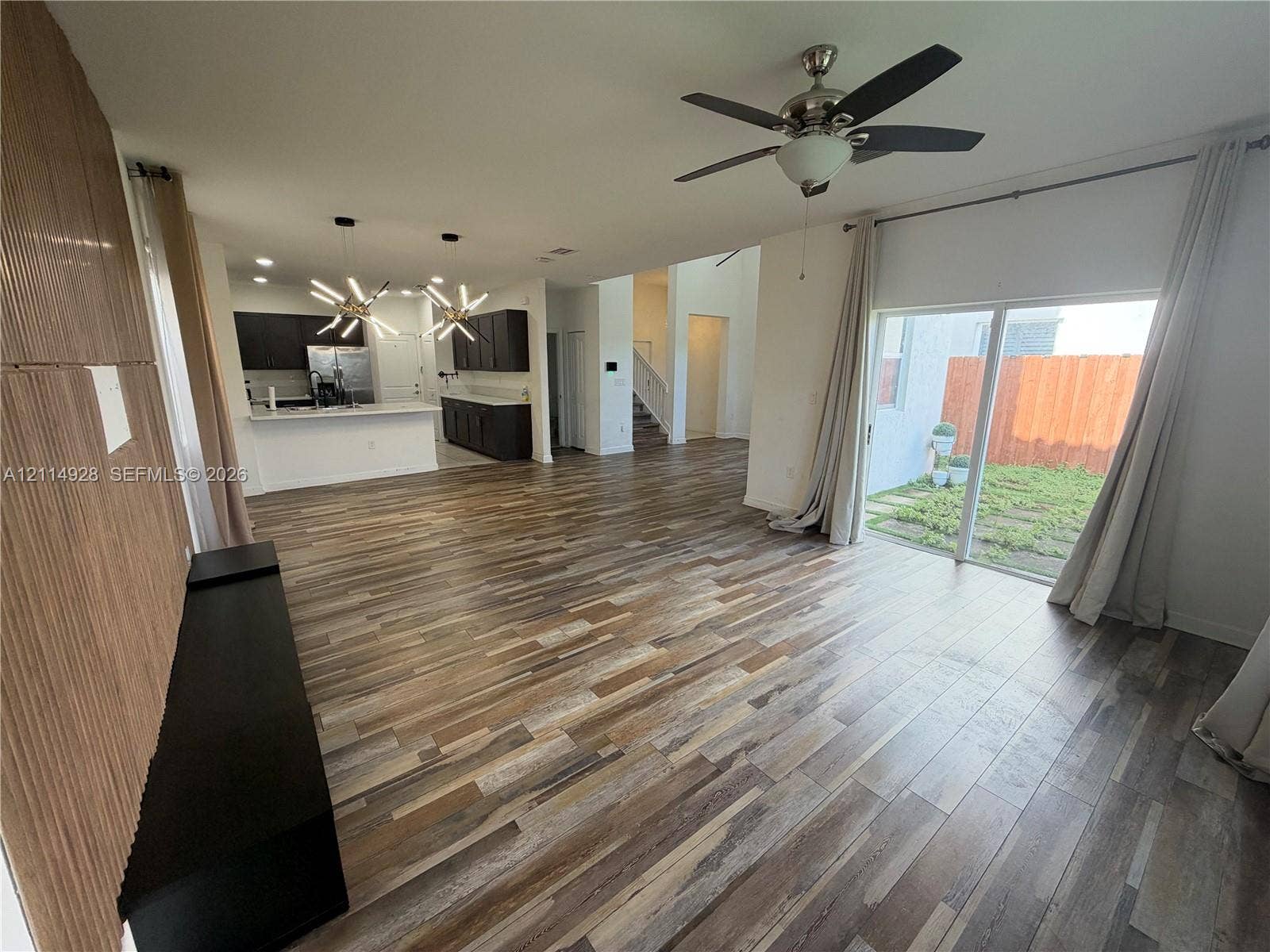 1411 SE 26th Road, Homestead, FL 33035 Wood-finish flooring throughout, kitchen featuring dark cabinetry and a peninsula, modern geometric pendant lighting, ceiling fan, and sliding glass doors