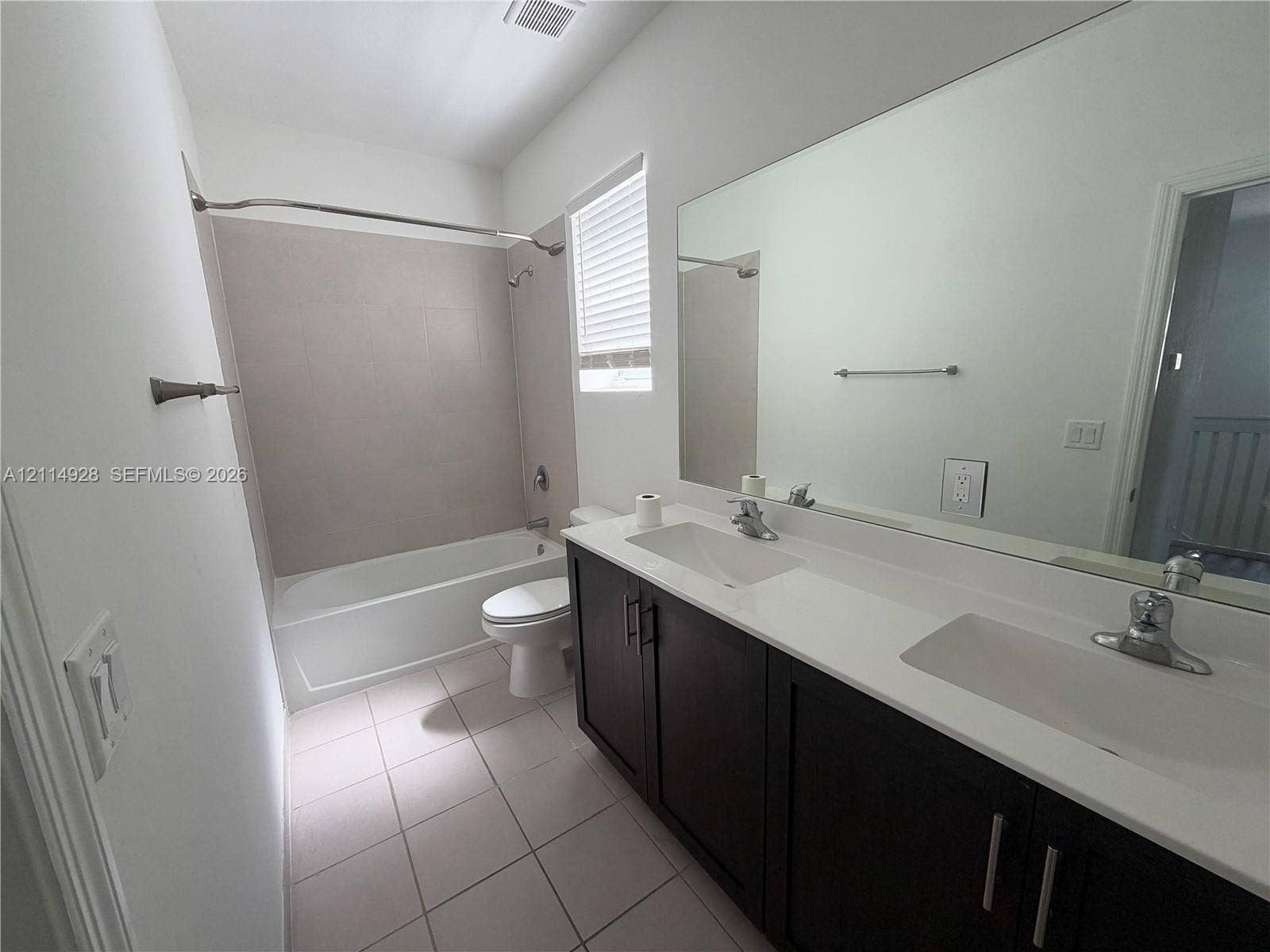 1411 SE 26th Road, Homestead, FL 33035 Bathroom featuring a dark-finish dual-sink vanity with white countertops, large wall-mounted mirror, ceramic tile flooring, and a bathtub with tile surround