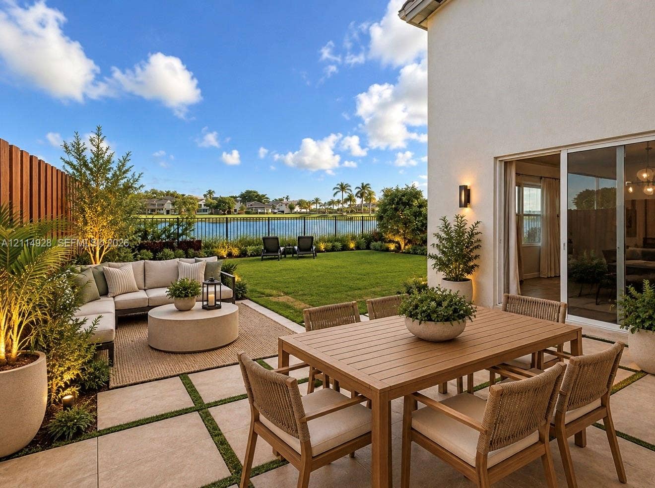 1411 SE 26th Road, Homestead, FL 33035 Rear patio featuring large-format pavers with grass inlay, manicured lawn, perimeter metal fencing, and wall-mounted exterior lighting