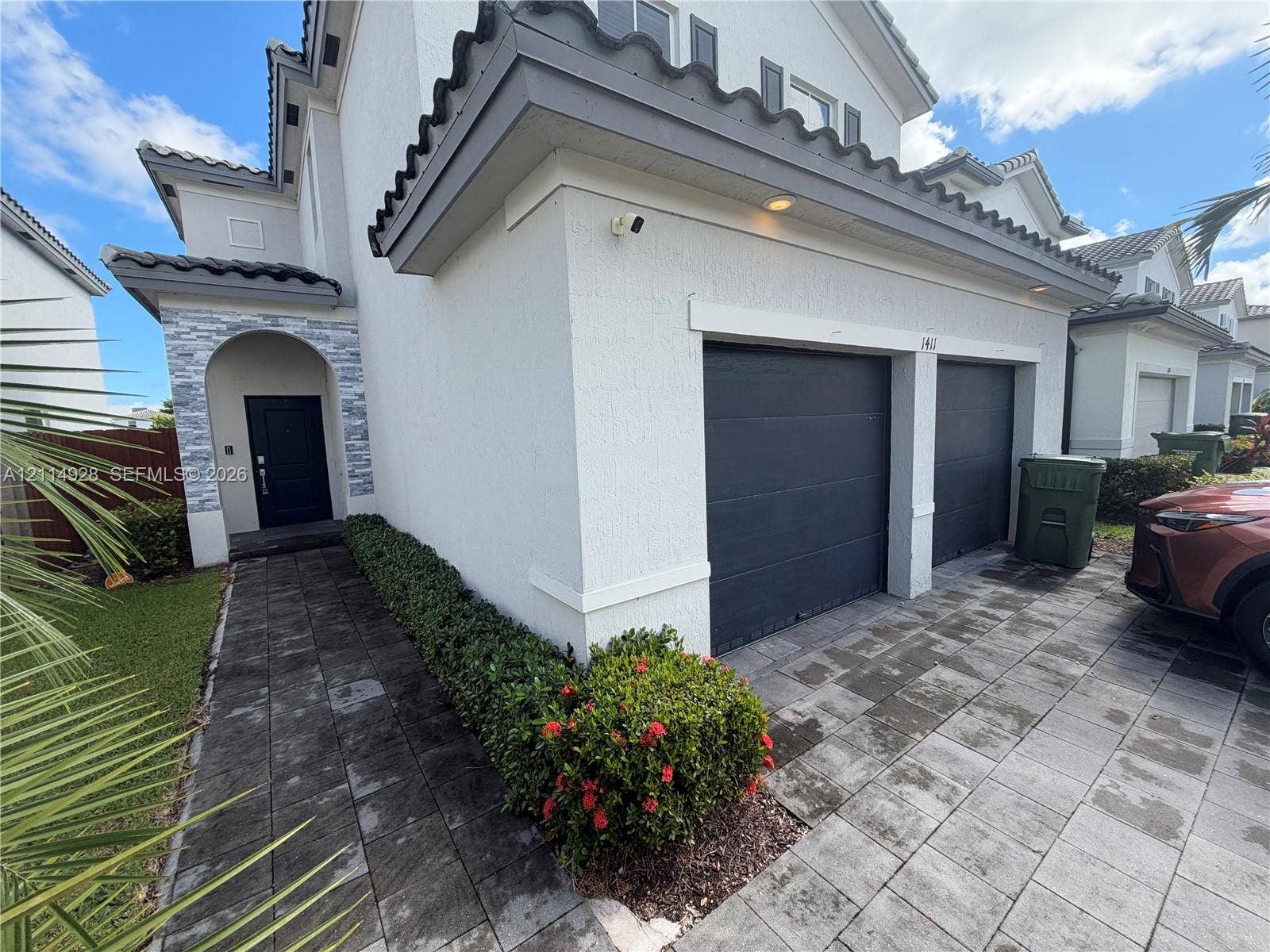 1411 SE 26th Road, Homestead, FL 33035 Two-story exterior featuring a stone-accented recessed entryway, paved driveway, and two-car garage with dark-finish doors