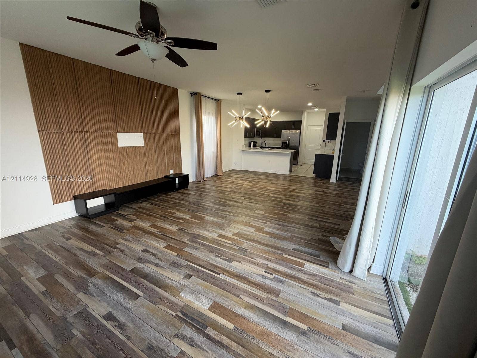 1411 SE 26th Road, Homestead, FL 33035 Open-concept interior featuring wood-finish flooring, a decorative vertical slat accent wall, a built-in low-profile media console, modern multi-arm light fixtures, and a ceiling fan