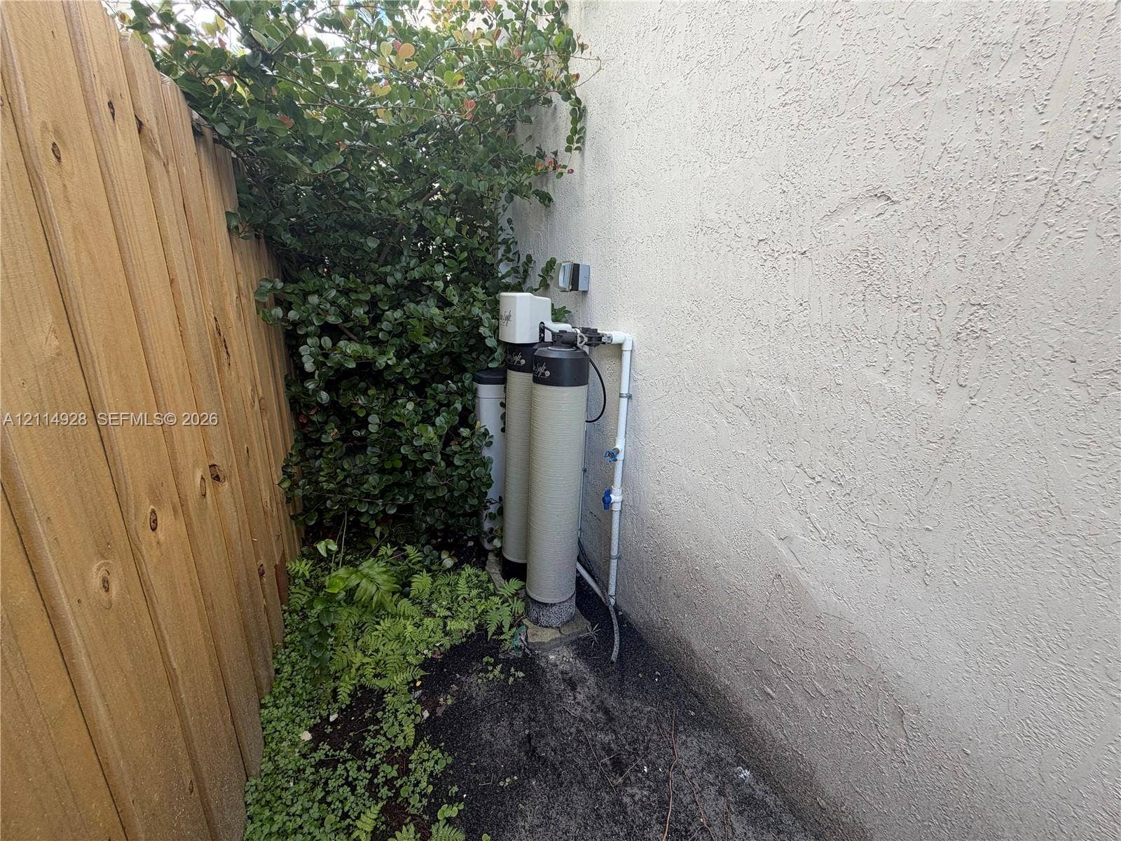 1411 SE 26th Road, Homestead, FL 33035 Water filtration system mounted to the exterior wall, enclosed by a wood-plank fence and mature landscaping