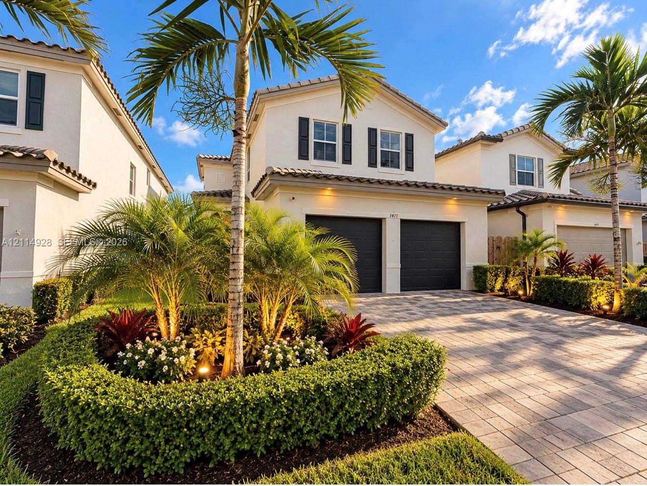 1411 SE 26th Road, Homestead, FL 33035 Two-story stucco exterior featuring a paver driveway, two-car garage, tile roofing, and mature palm tree landscaping