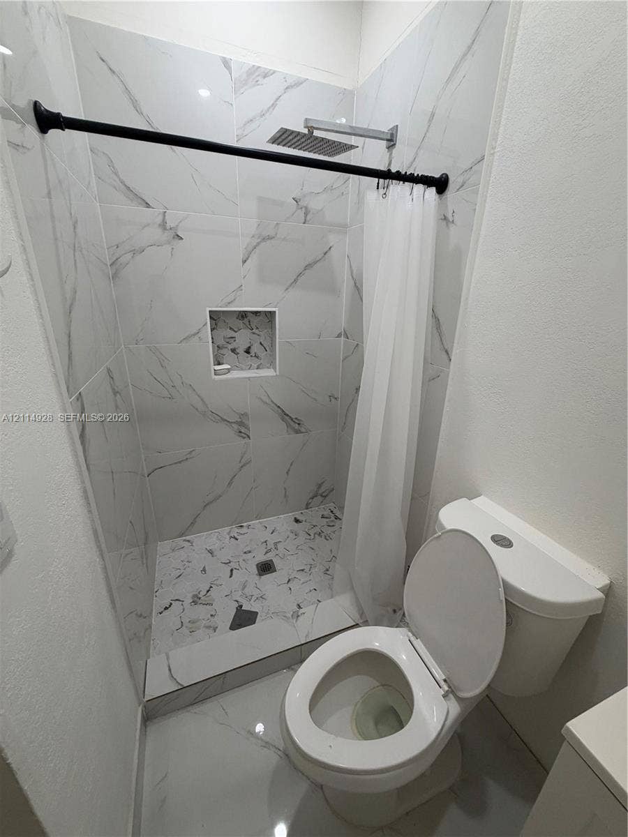 1411 SE 26th Road, Homestead, FL 33035 Shower featuring large-format veined tile surround, recessed wall niche, rain-style shower head, and matte black hardware