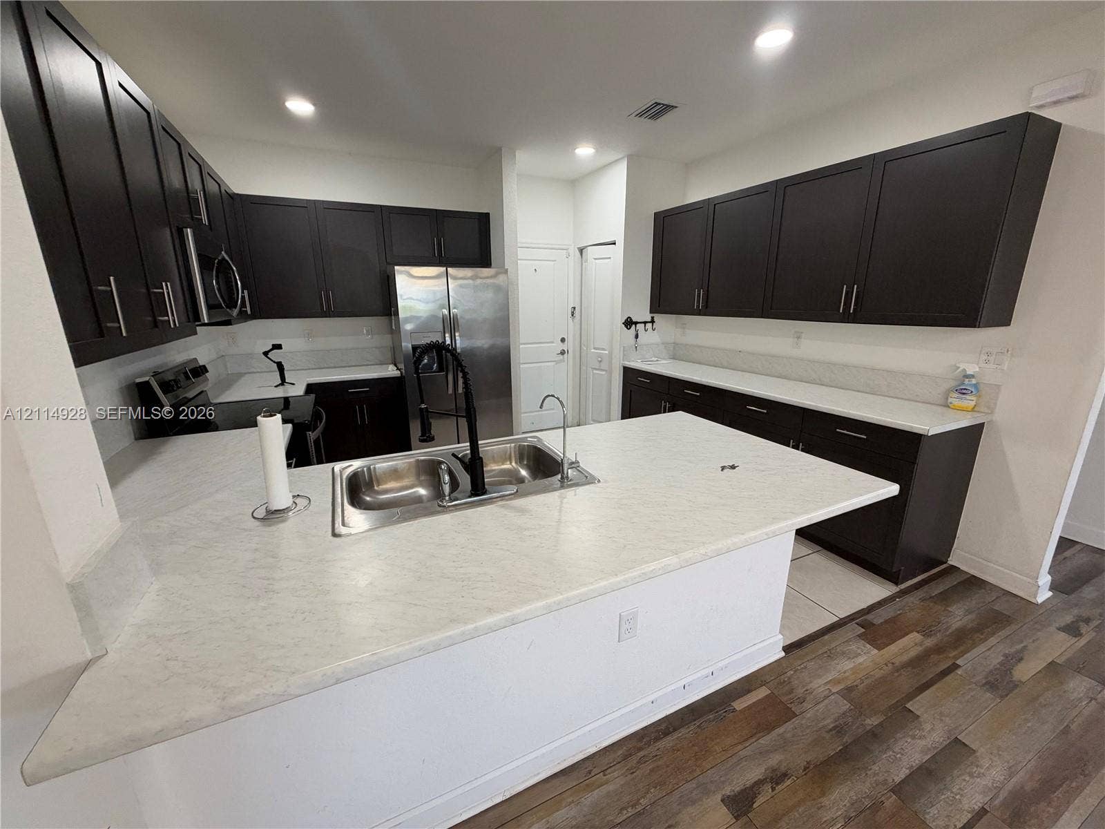 1411 SE 26th Road, Homestead, FL 33035 Kitchen featuring dark wood cabinetry, a central island with a dual-basin sink, light-toned countertops, stainless steel appliances, and wood-finish flooring